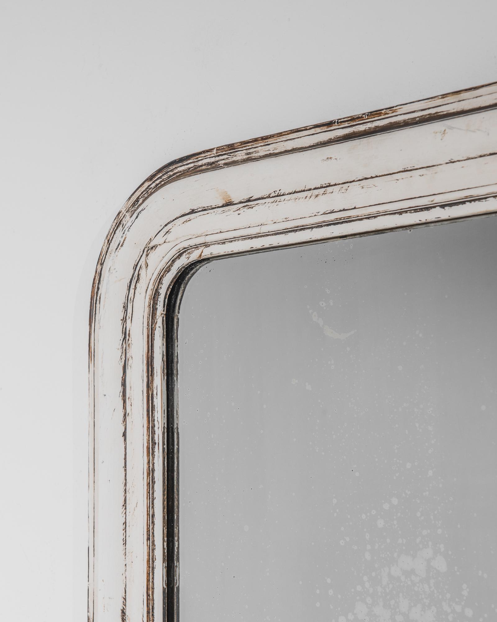 A wooden mirror from 1880s France. The curved upper corners of the frame create a softly rounded profile, harmonizing with the pale dove grey of the paint. A subtle patina reveals the dark tone of the natural wood. Graceful lines and a calming color