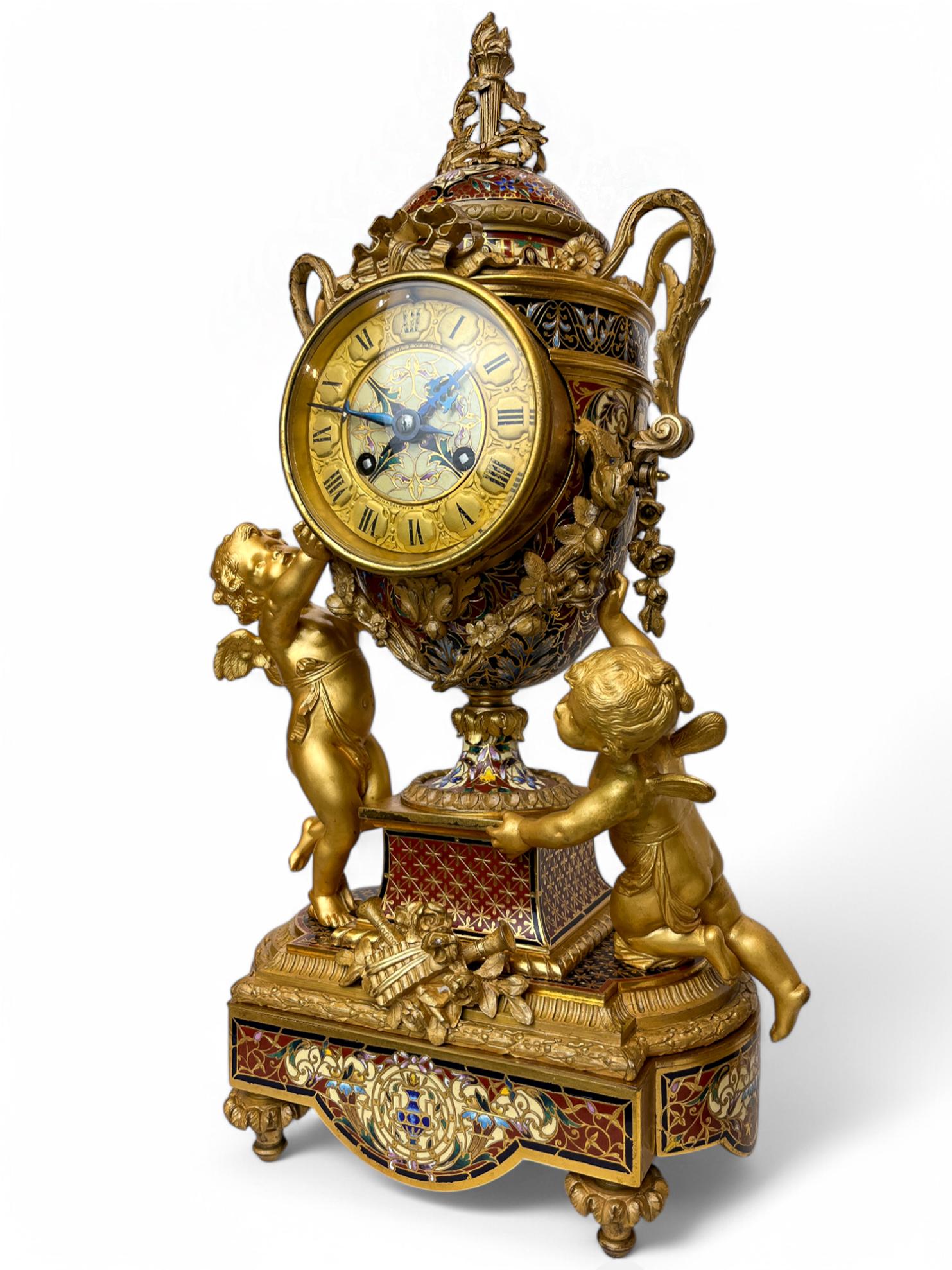 Napoleon III Gilt-Bronze and Champleve Enamel Mantel Clock retailed by J.E. Caldwell & Co paired Champlevé and Gilt-bronze Five-light Candelabras

A black and maroon enamel ornamented vase clock with roman numeral dial, mounted with gilt bronze