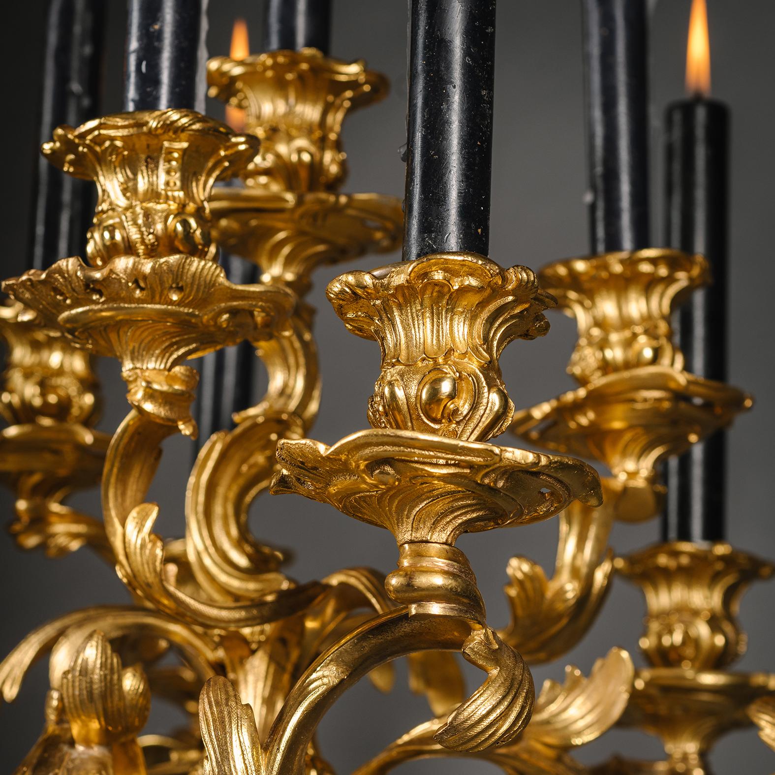 Ein Paar große Napoleon-III-Kronleuchter aus vergoldeter Bronze mit neun Lichtern, die die Jagd symbolisieren. 

Jedes Stück ist im Stil Ludwigs XV. konzipiert und hat einen Rocaille-Stiel, der assymetrisch modellierte, gerollte Branches trägt. Der