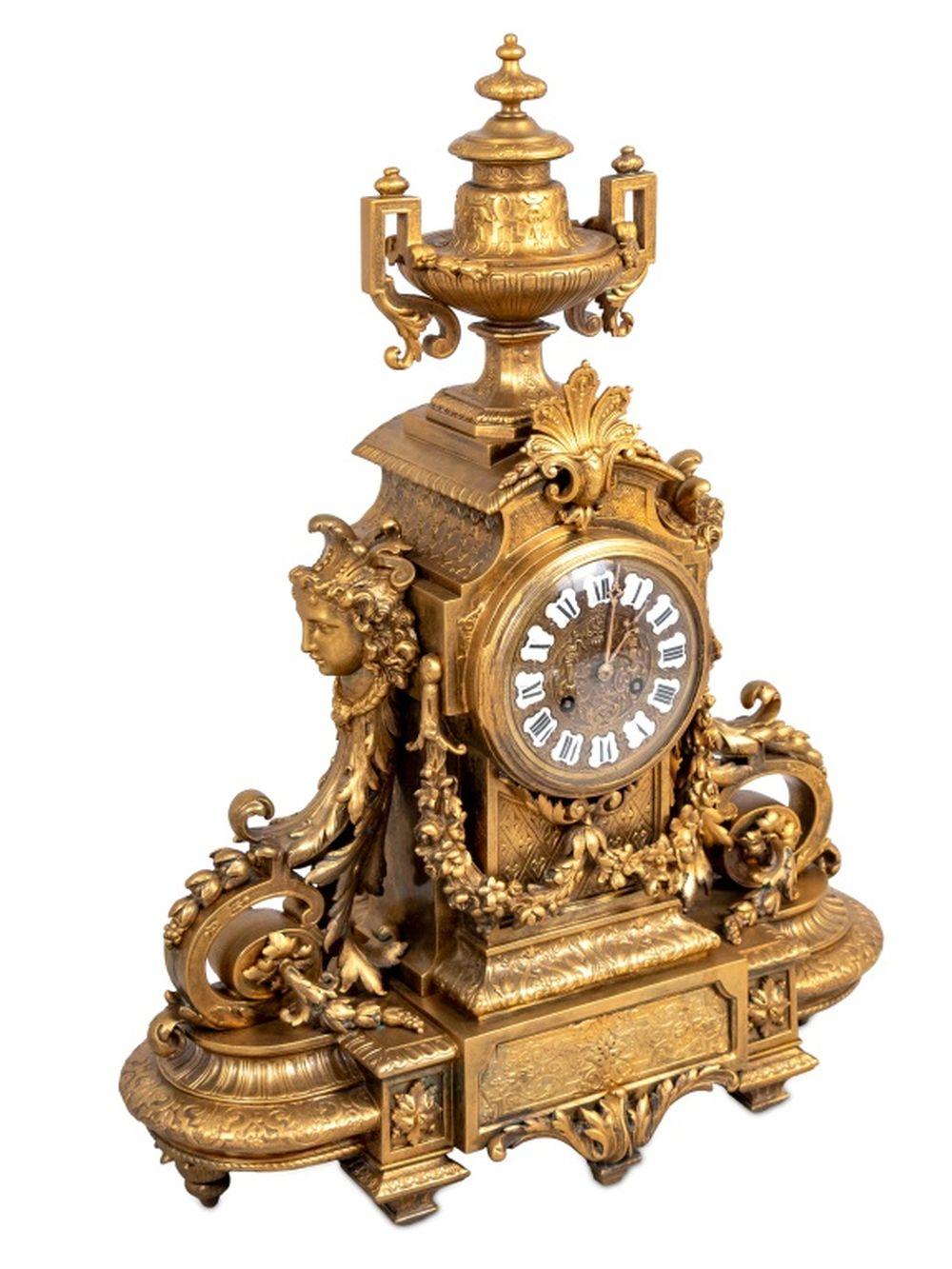 Napoleon III Gilt Bronze Three-Piece Clock Set, circa 1870, comprising: a clock surmounted by two-handled urn with a circular dial inset with enameled numerals, with acanthus scrolls, figural supports, on an oval base, together with a pair of six