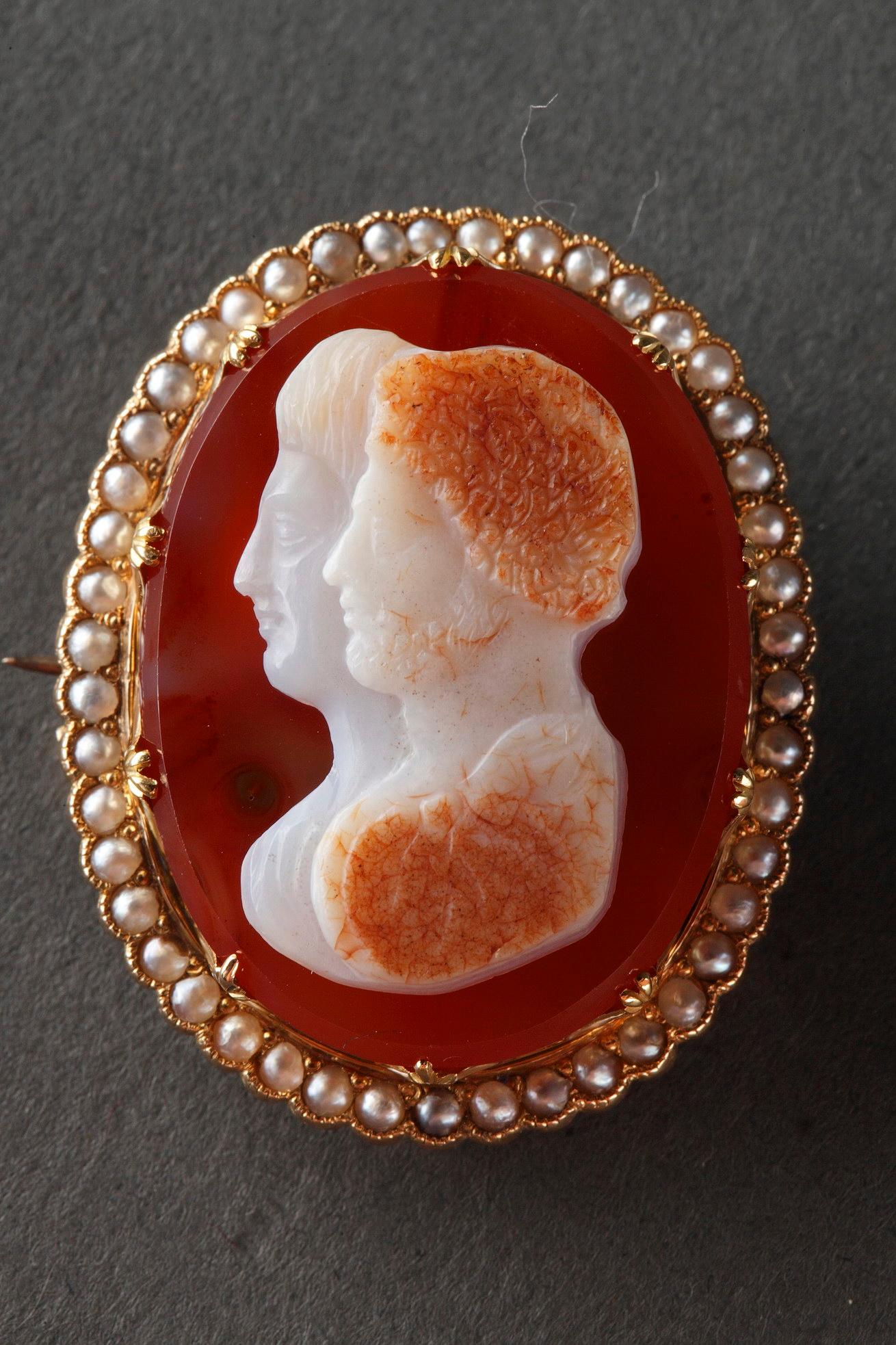 9th century agate cameo brooch, set in gold mounting. It shows two busts of Marcus Aurelius and Faustina in profile, raised in low relief on a dark red background. The gold mounting is set with a row of small pearls.
 
Dim: W: 1 in – D: ,4in – H: