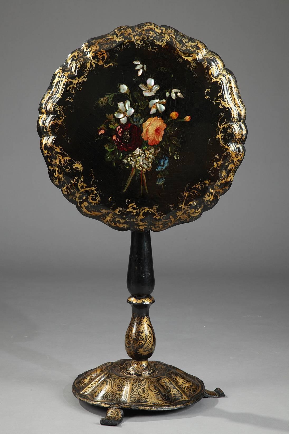 Small gueridon in wood and lacquered cardboard. The tabletops scalloped border and round base are decorated with gilded foliage and scrollwork, while painted flowers inlaid with mother of pearl embellish the center of the table. A balustrade-shaped