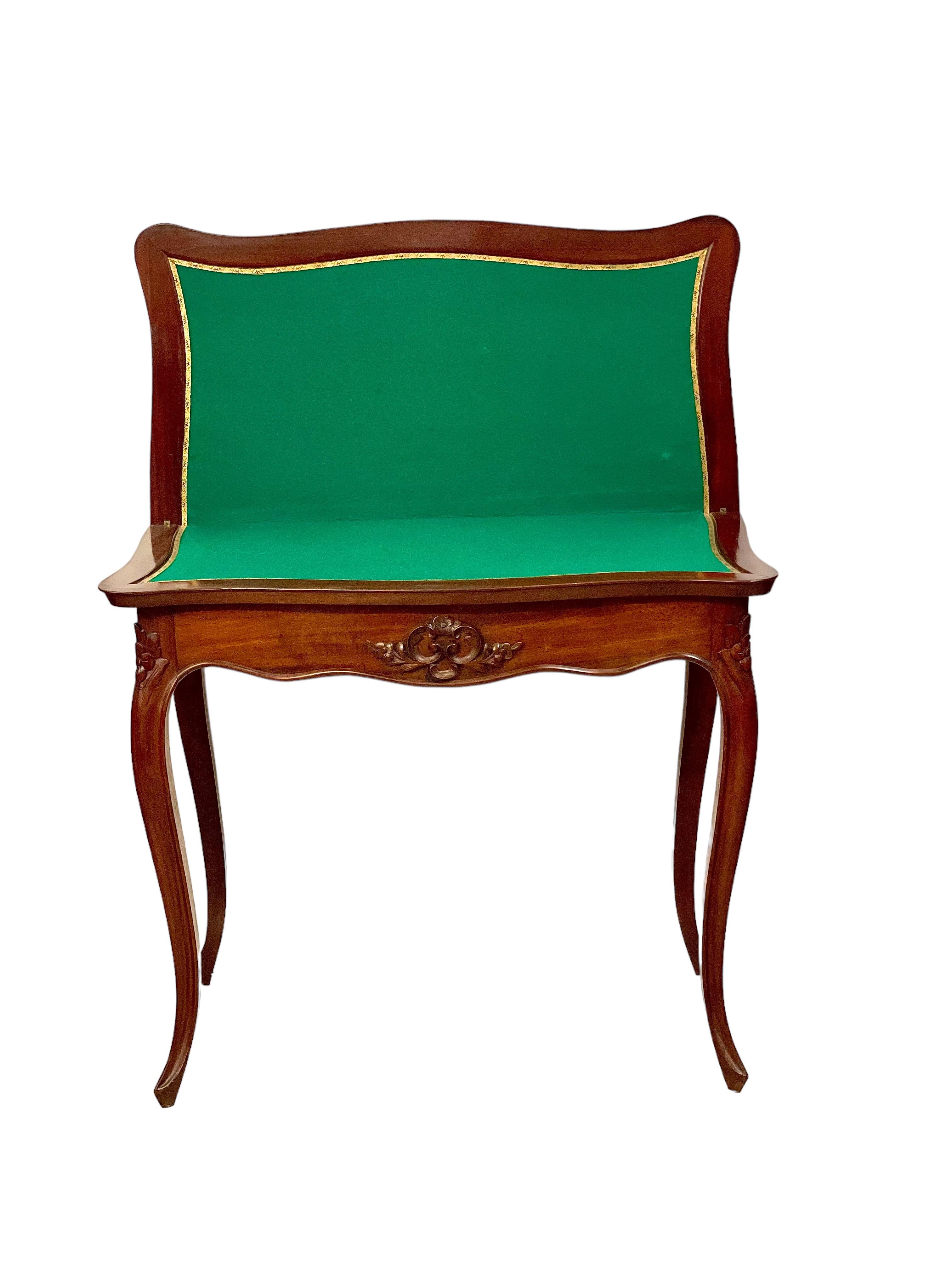 An elegant 19th century Napoleon III-era Fruitwood gaming table, featuring an intricate moulded flourish on its front apron and beautifully carved roses at each shoulder. The top of the table is hinged, and opens to reveal a shaped, green baize