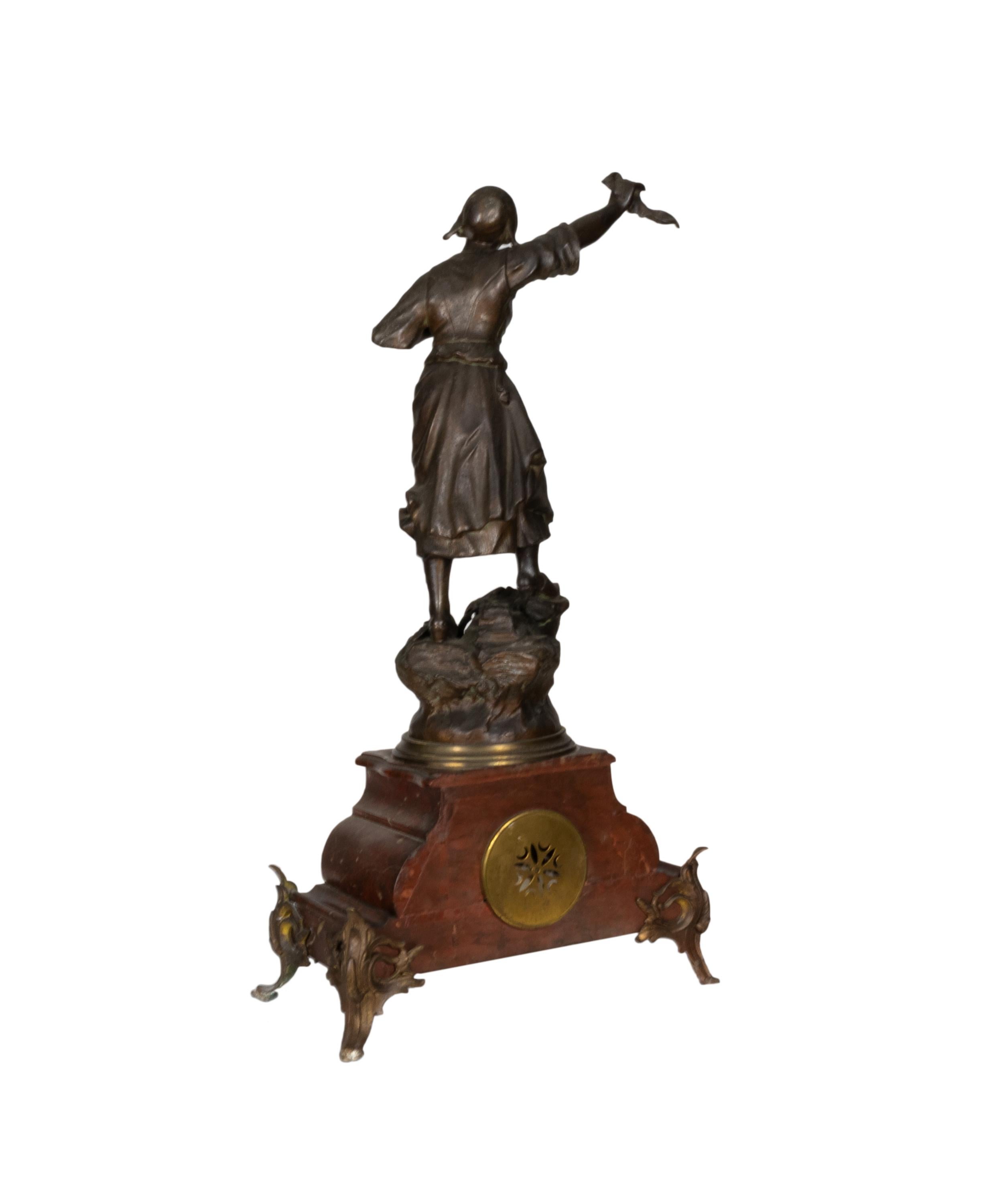 A Napoleon III mantel clock featuring a dynamic sculpture of a Revolutionary French peasant woman. 

Made from high-quality metal and adorned with rich red marble accents, this timepiece is a true work of art, showcasing intricate details and