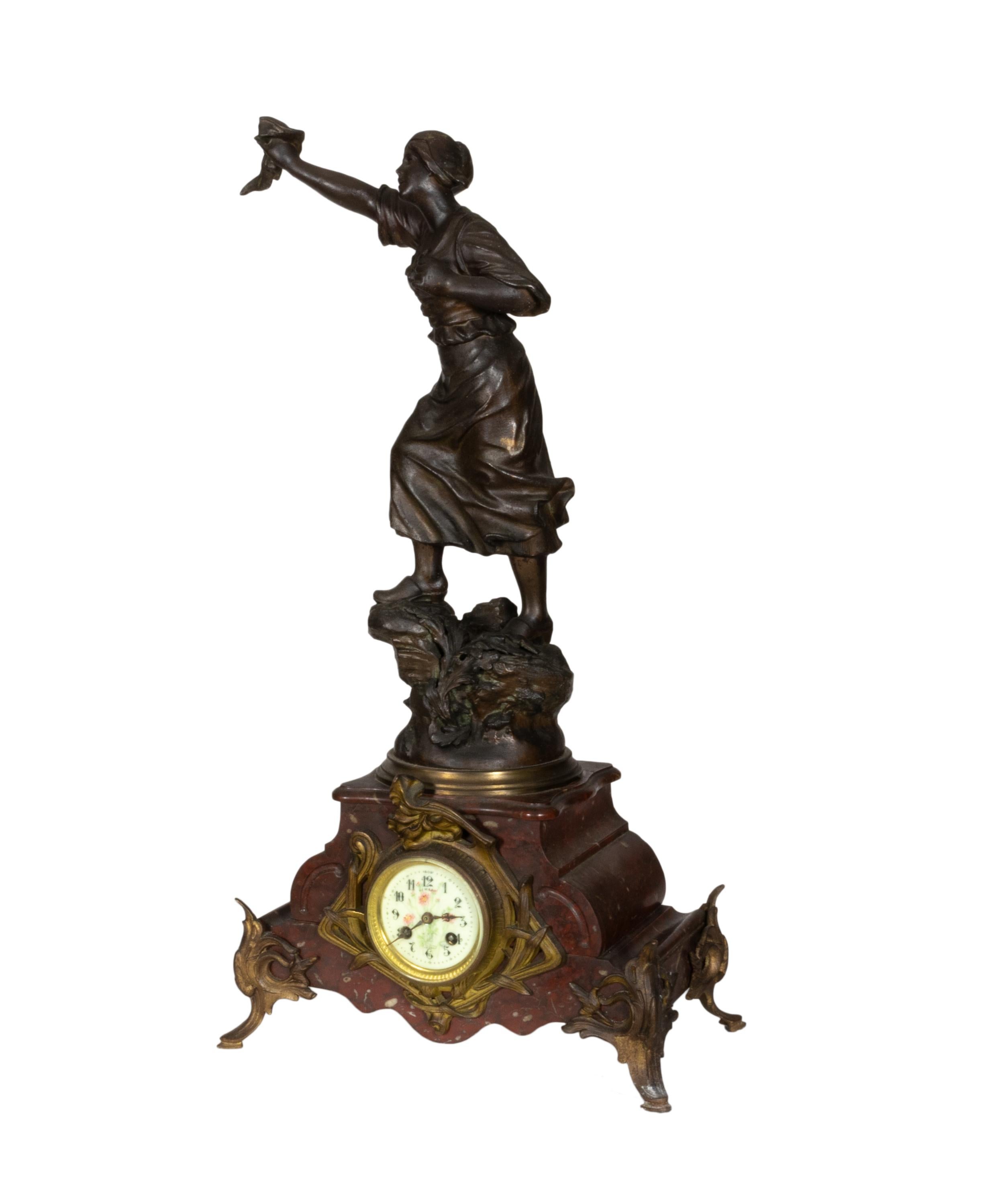 A Napoleon III mantel clock featuring a dynamic sculpture of a Revolutionary French peasant woman. 

Made from high-quality metal and adorned with rich red marble accents, this timepiece is a true work of art, showcasing intricate details and
