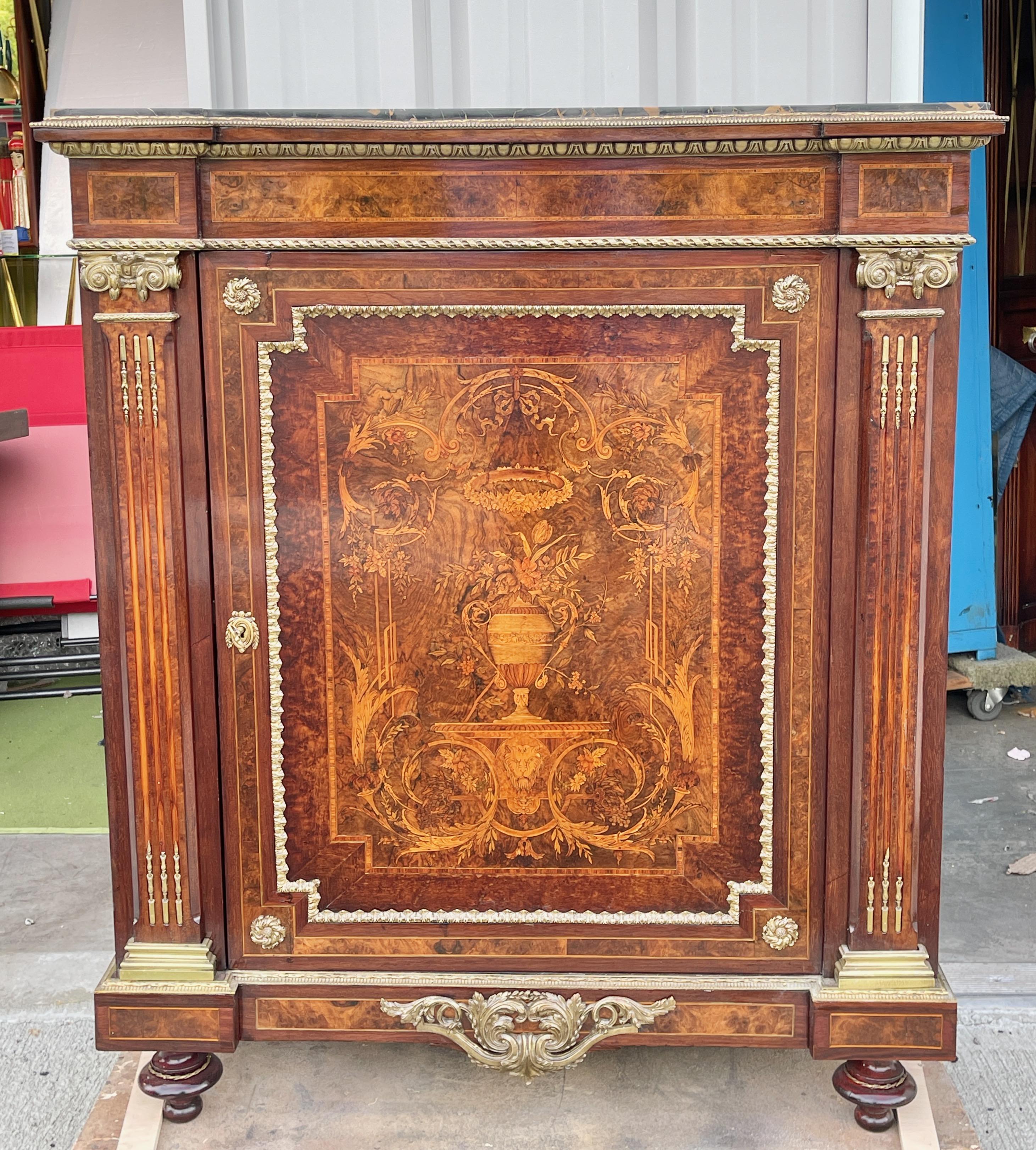 Cabinet de salon Napoléon III en marqueterie de bois de roi, de satin et de bois fruitier, surmonté d'un plateau en marbre noir veiné, avec moulures et montures en laiton doré. Deux étagères réglables. La serrure et la clé fonctionnent.