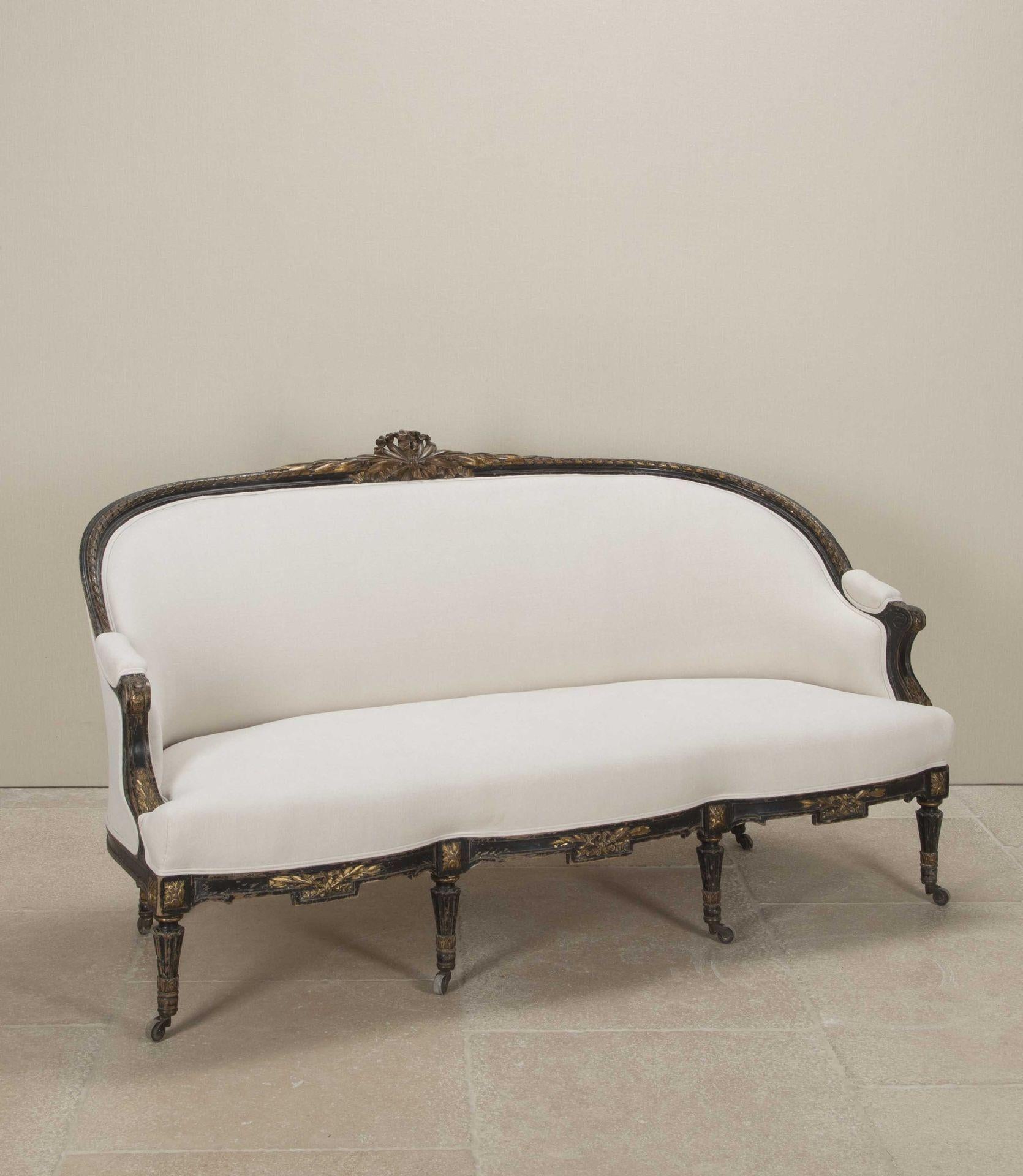 An elegant Napoleon III period French sofa or canape. The ebonised frame with gilded carved details has a corbeille form with down-swept arms and a serpentine front. It has been newly recovered in an off-white vintage French linen.