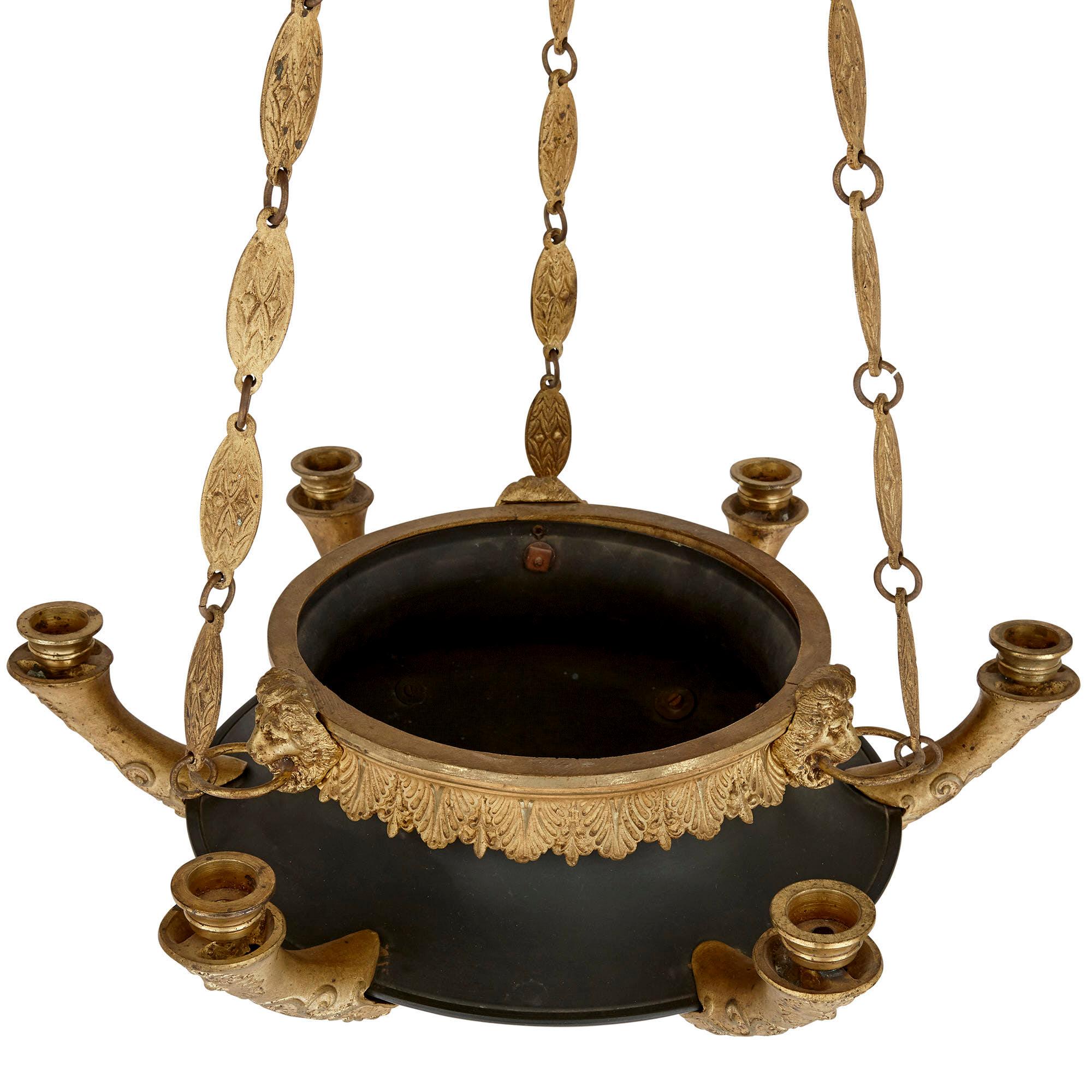 This unusual chandelier is designed in the Empire style from gilt and patinated bronze in the form of an ancient Roman terracotta or earthenware oil lamp. The patinated bronze bowl of the lamp is open at the top, the top rim mounted with ornately