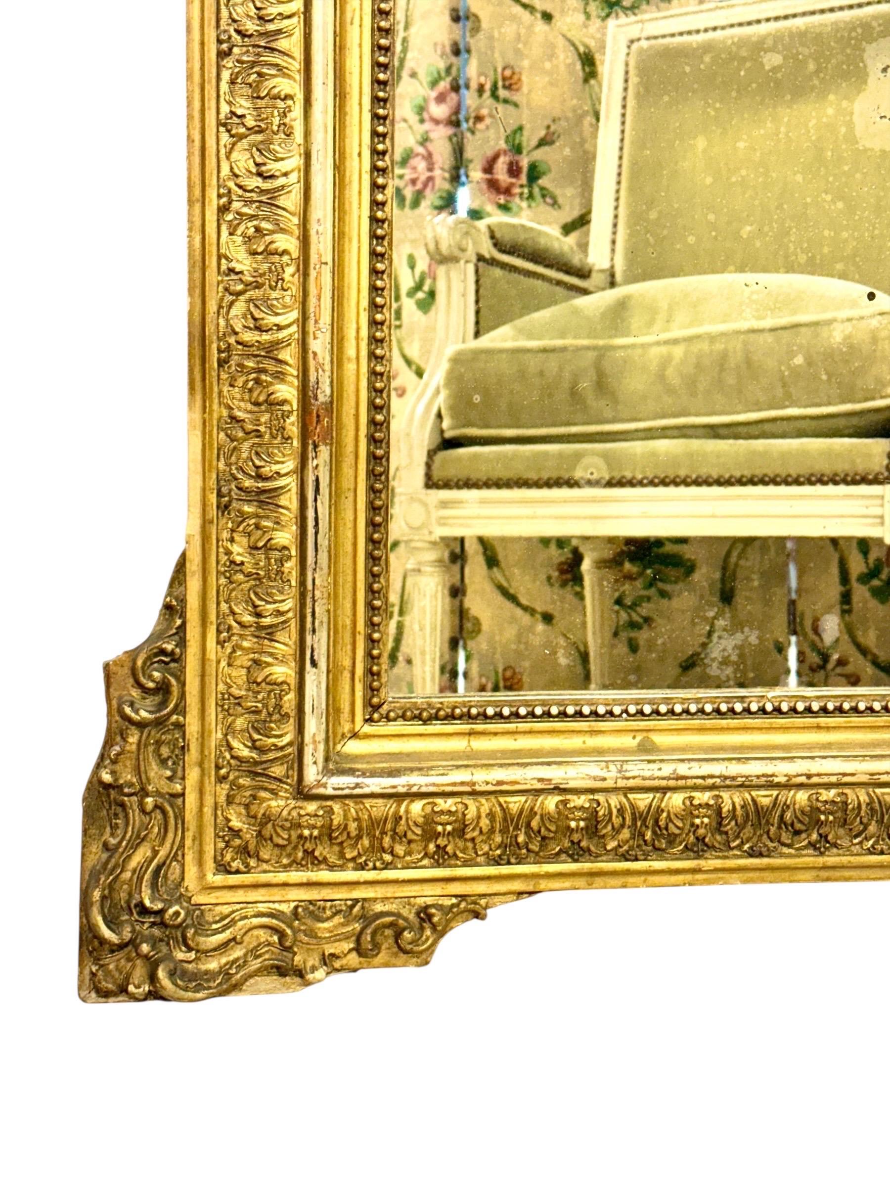 Questo splendido specchio francese del XIX secolo emana opulenza e grandezza, con una cornice in legno riccamente intagliata e dorata che mostra la migliore maestria artigianale del periodo di Napoleone III. Lo stemma è coronato da un elaborato