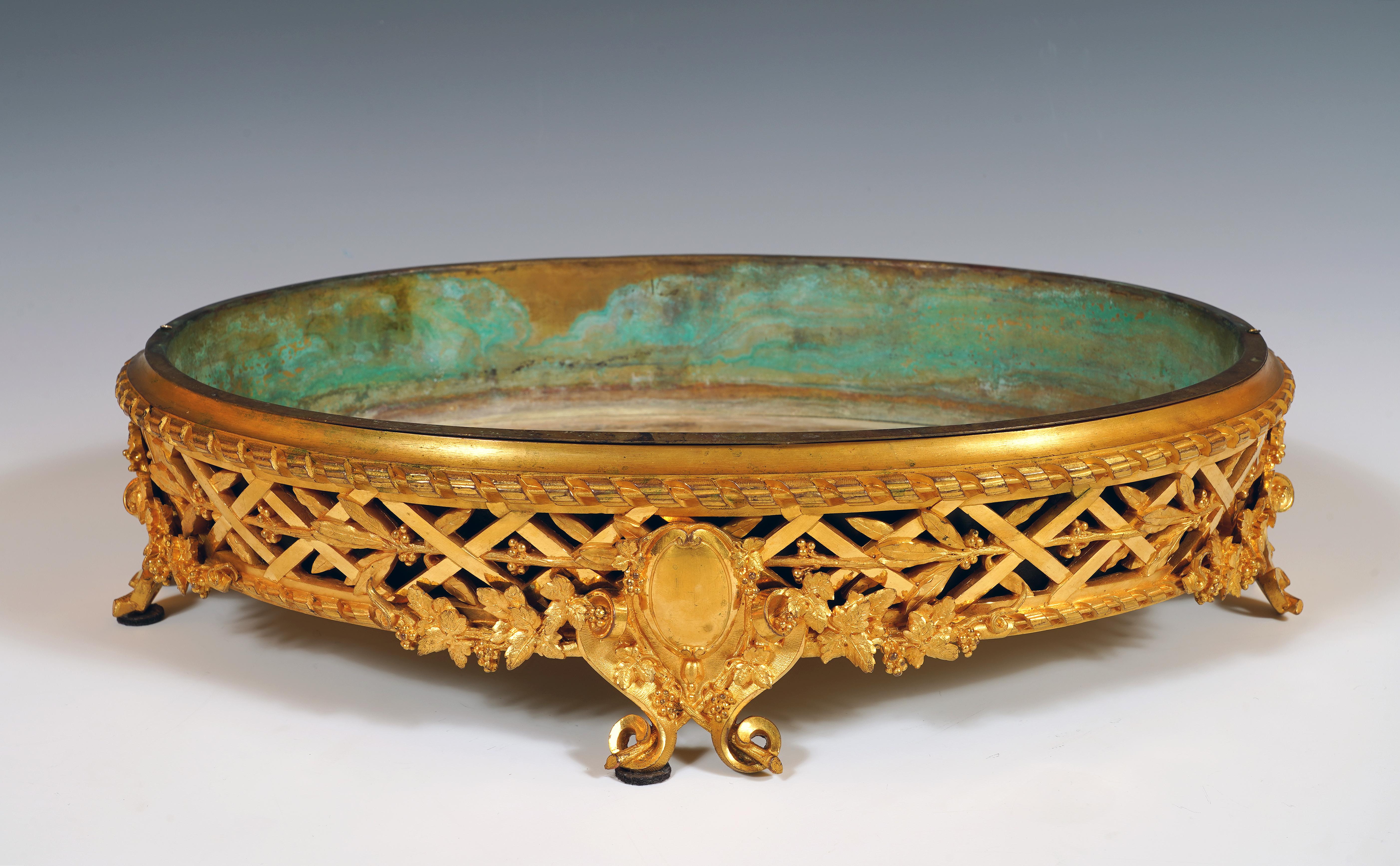 Signé MASSELOTTE et numéroté 1064

Elegante jardinière ovale Napoléon III en bronze doré, à bord décoré de croisillons entrelacés de feuilles de laurier. Il repose sur quatre pieds en forme de cuir découpé orné de branches de vigne, portant un