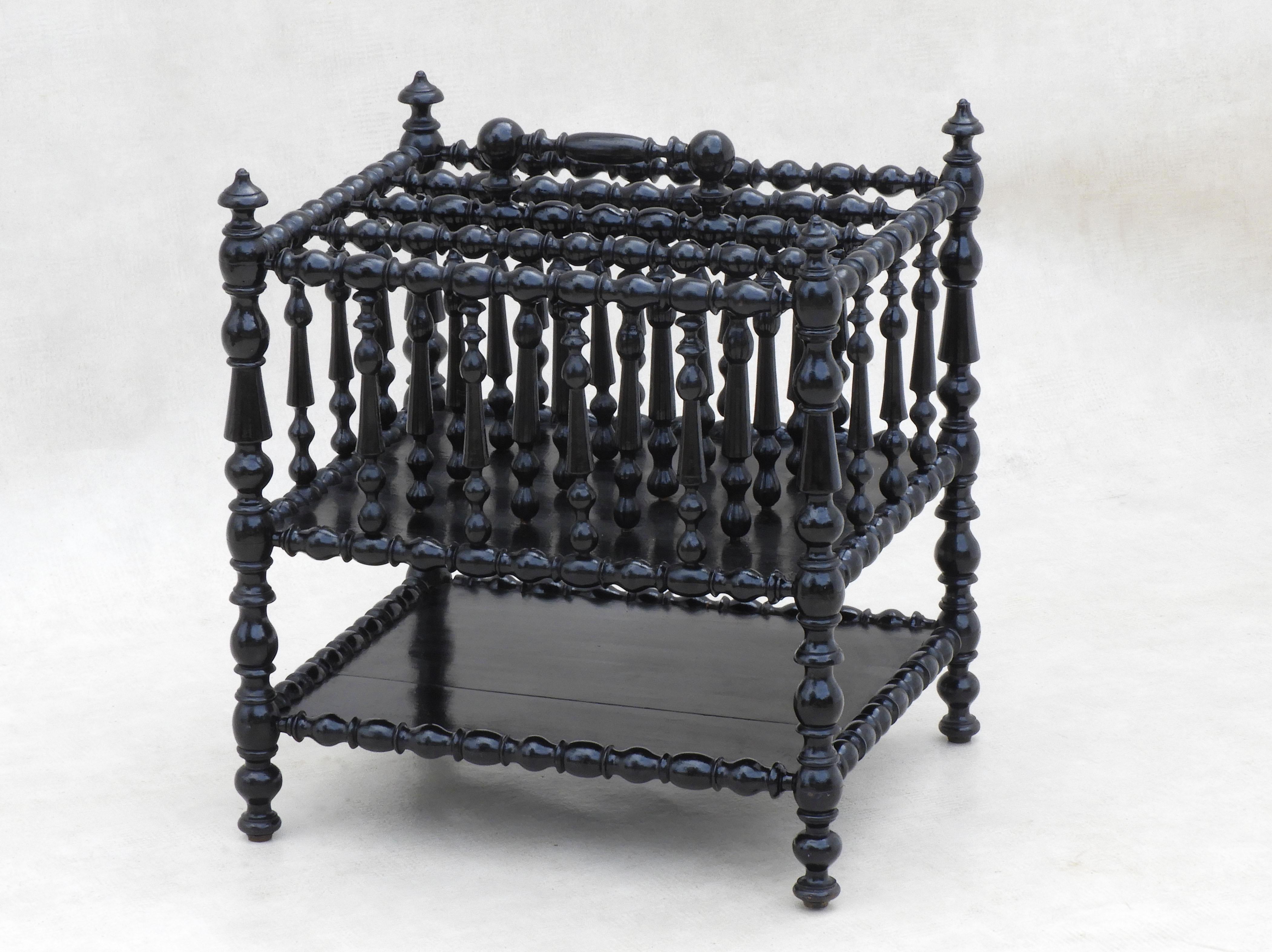 Stylish French Napoleon III 'porte revue' magazine rack or canterbury. Black lacquered and beautifully turned wood, this 
four-sectioned stand with an undershelf, and carrying that handle, will work well within a diverse range of interior styles.