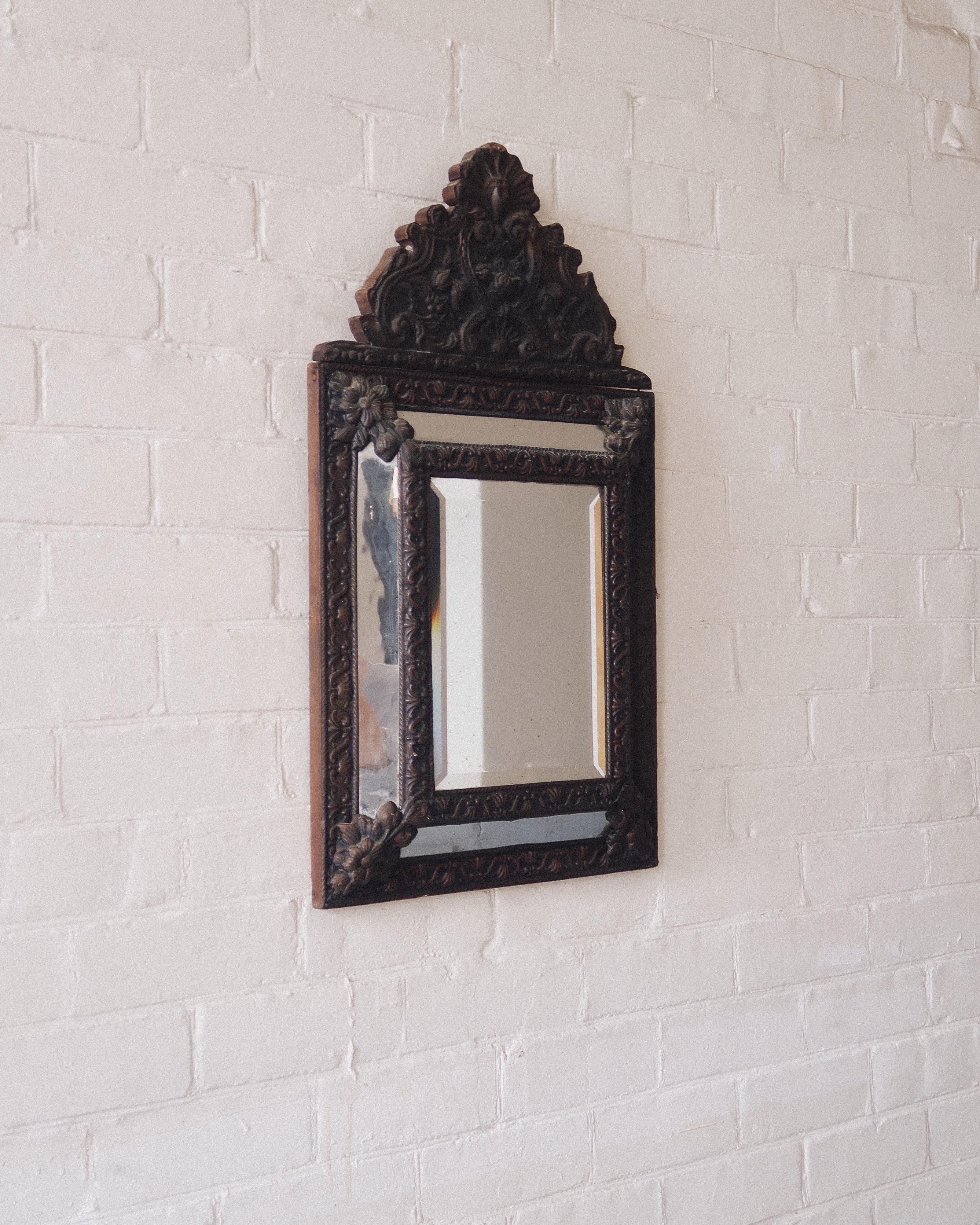 French, 19th century. A mirror that doesn’t do minimal. The central beveled glass is framed by four rectangular panels, joined with repoussé brass floral motifs. The filigree crest is all flourish, with sculptural foliage details carrying through to