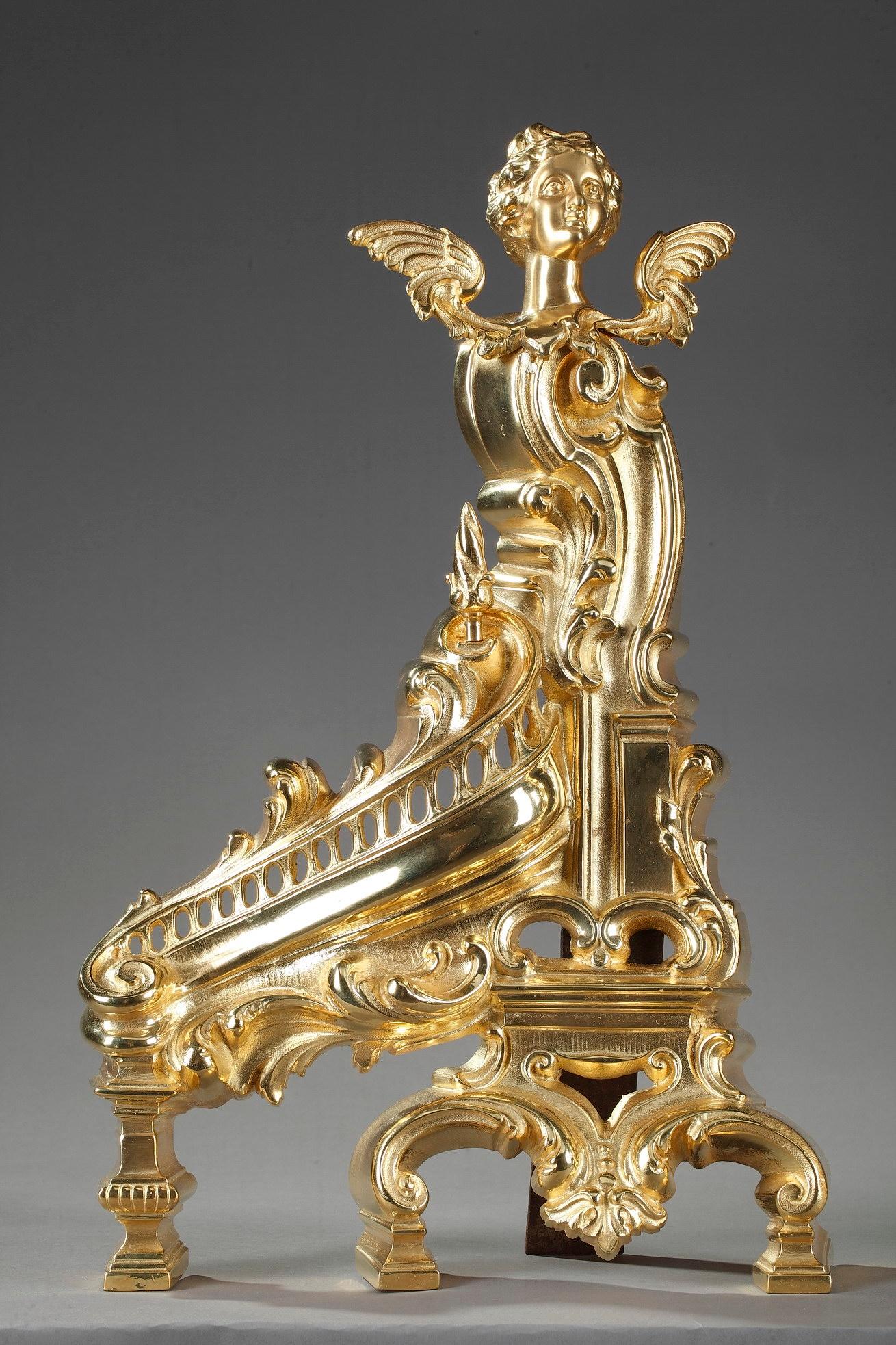 Pair of gilt bronze andirons with rich rococo decoration such as acanthus leaves, pierced ova and exuberant scrollwork. They are topped by two majestic winged women. Andirons, or chenets, are decorative and practical objects placed in front of a