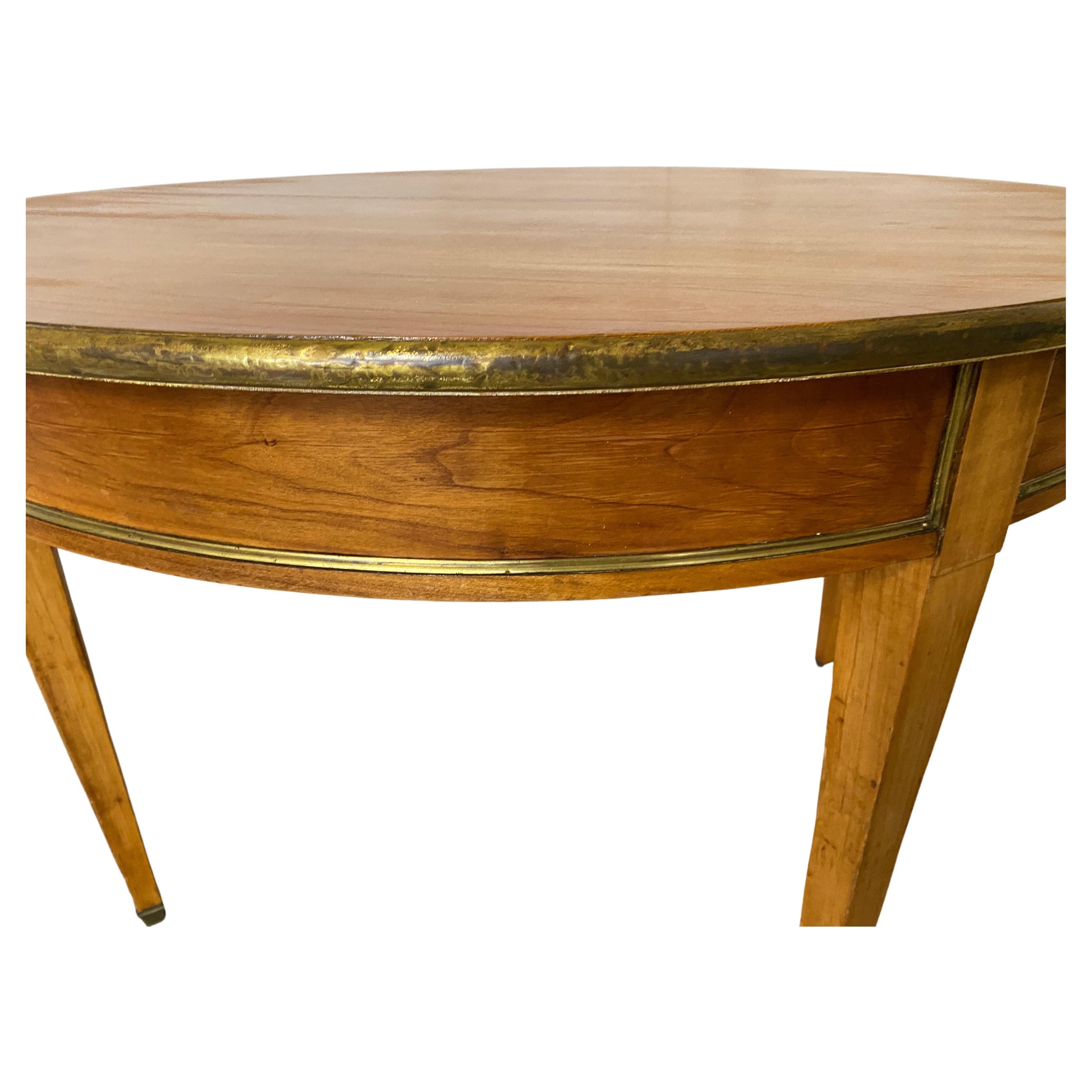 19th century fine circular dining table with all around brass trim and a thinner one on the lower edge of the skirt, tapered leg terminating in brass casters. Strong Viennese Biedermeier or Neo-Classical influence. The simplicity of design and light