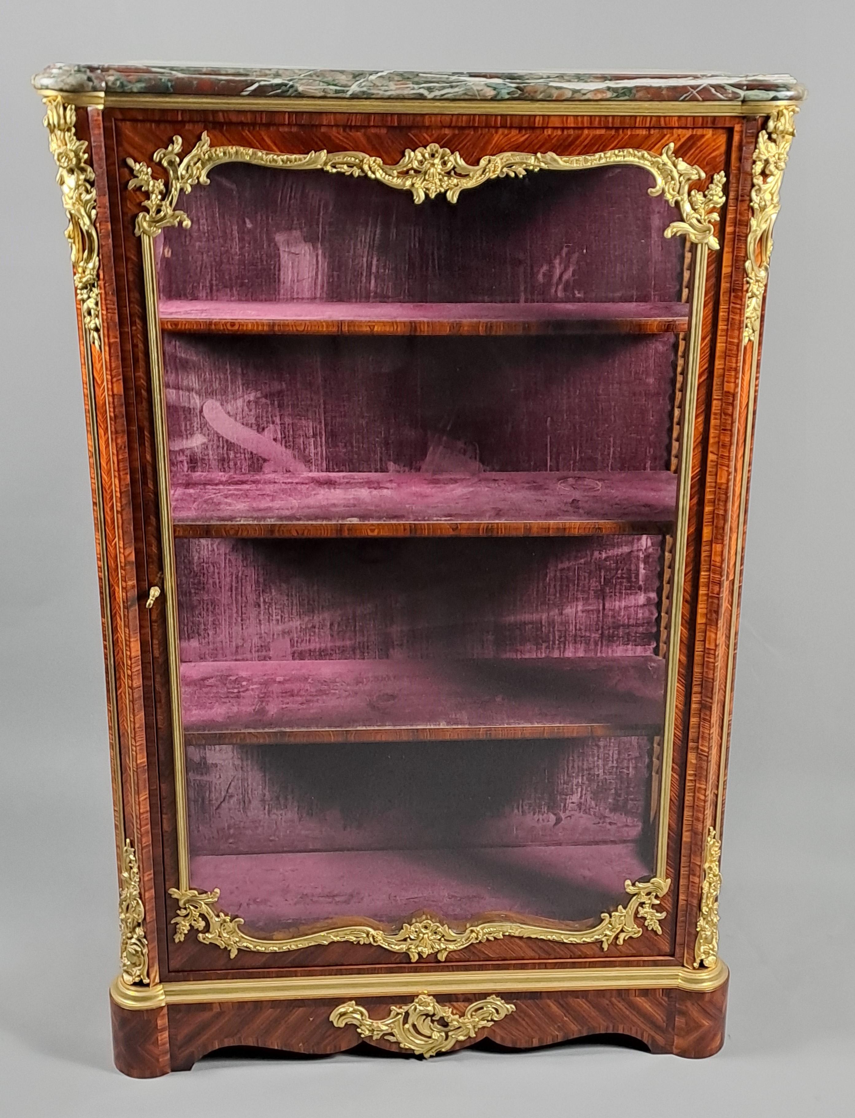 Magnifica vetrina in legno intarsiato viola con ricchi ornamenti in bronzo dorato, finemente cesellata con motivi di ispirazione Luigi XV.   

Il piano è ricoperto da un marmo Campan Grand Mélange, modellato in un doppio bec de corbin. 