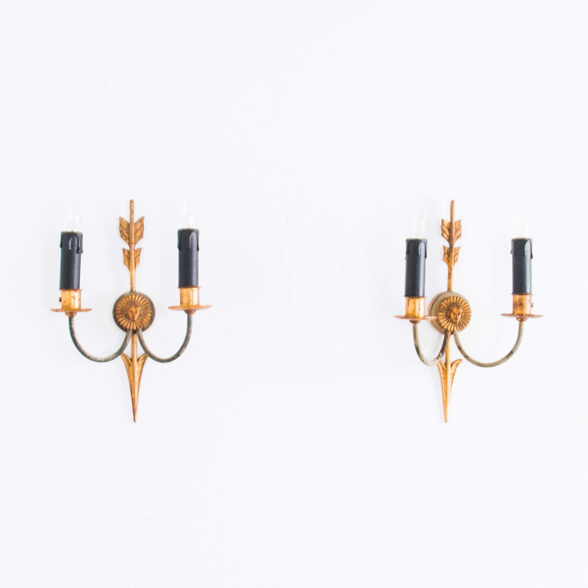 This pair of Second Empire style wall sconces from turn of the century France provide a handsome antique light source. The backplates take the form of a golden arrow piercing a radiant emblem, from which emerge a pair of curved symmetrical arms.