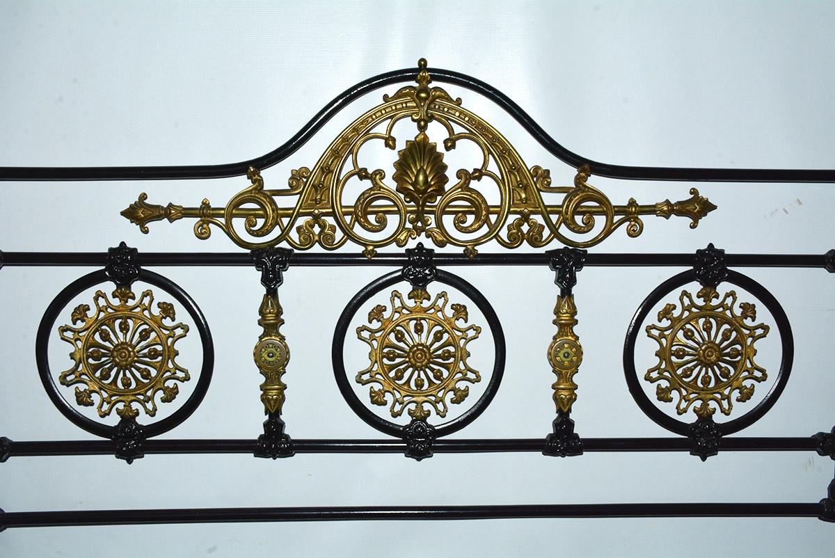 Napoleon III style king bed headboard is constructed of iron and bronze painted black with elaborate solid brass detailing, including filigree rosettes and pediments. The outer posts and legs have a scattering of hand painted pansies and leaves.
