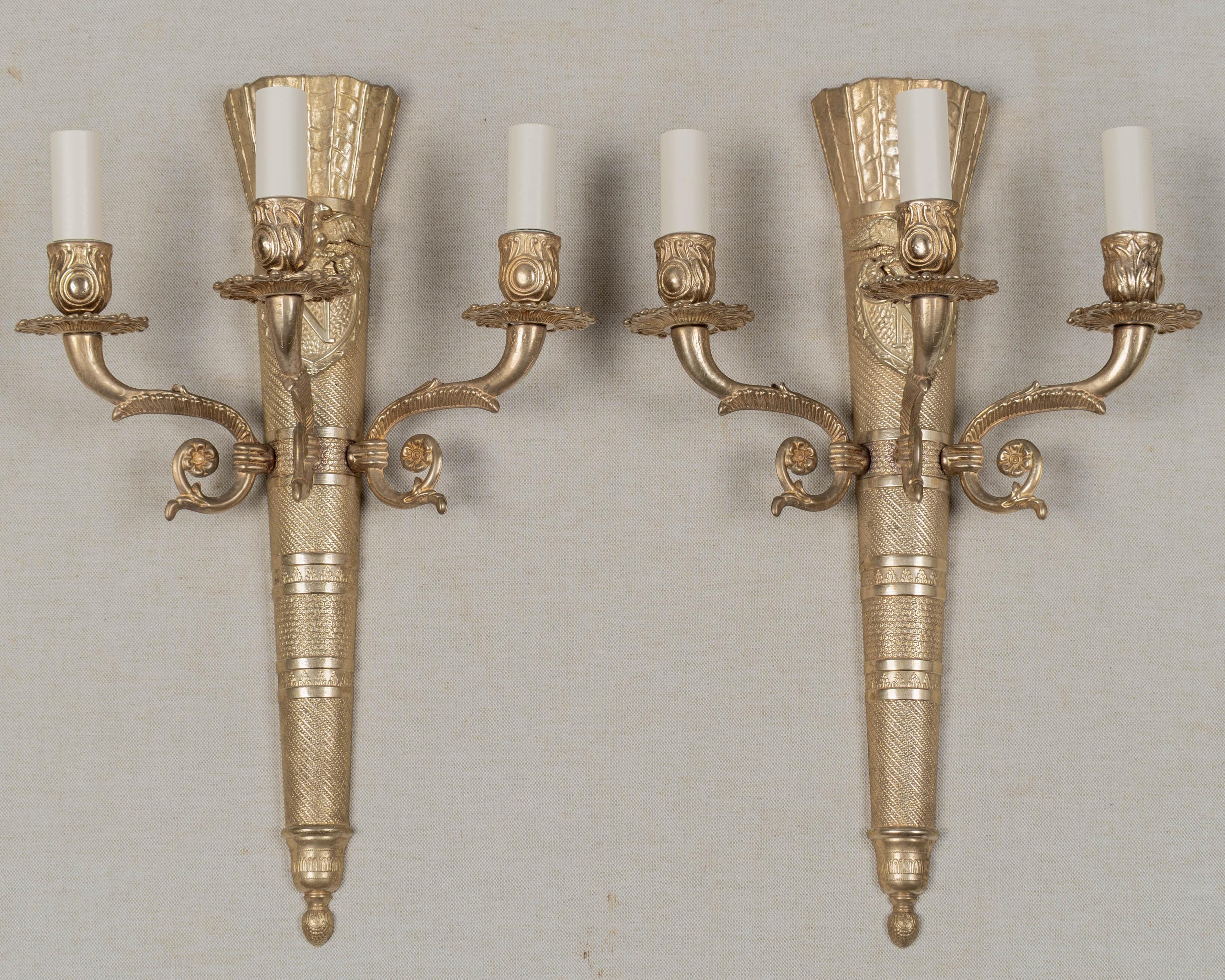 Coppia di appliques francesi in bronzo fuso dell'inizio del XX secolo in stile Napoleone III, ciascuna con tre bracci a voluta. Forma classica a forma di faretra di frecce con stemma applicato con un'aquila e l'iniziale N. Superficie finemente fusa