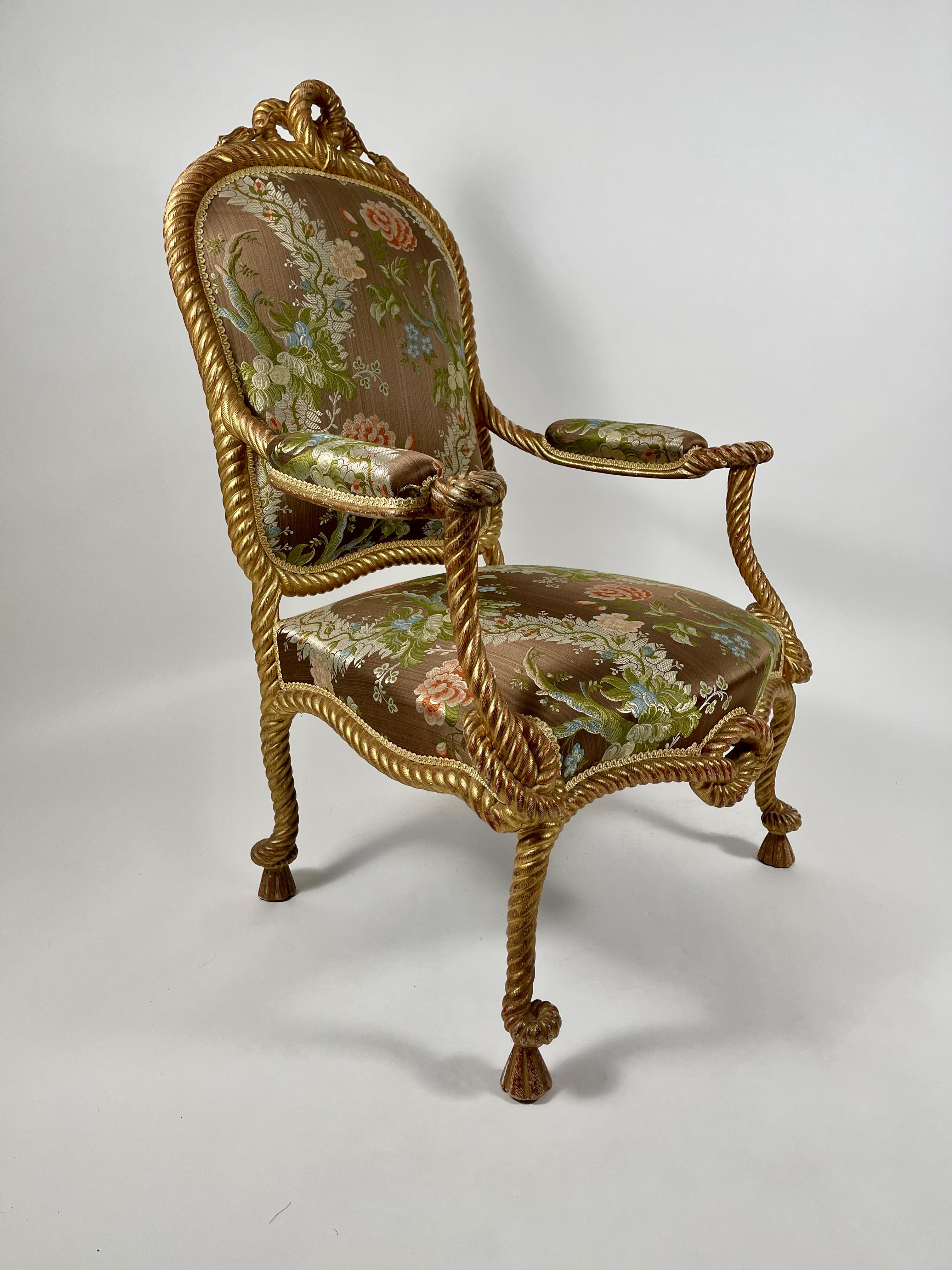 A fine quality Napoleon III style carved and gilded rope and tassel armchair, the shaped upholstered back with a knotted and tasseled crest. Its entire frame, from partially upholstered arms to seat rail, legs and feet, are all very well carved to