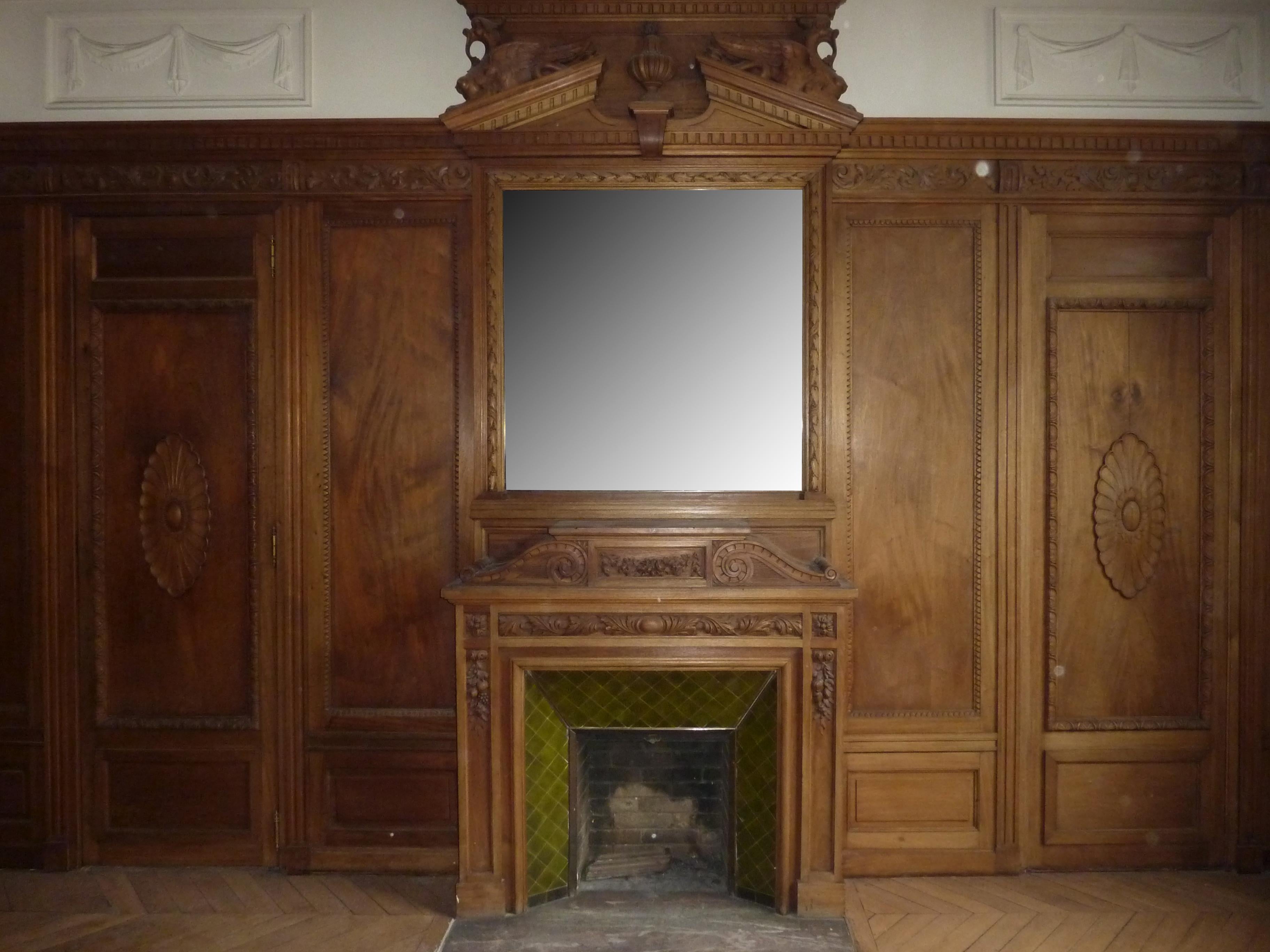 Pièce de boiserie de style Napoléon III réalisée au XIXe siècle en bois de noyer sculpté provenant du salon d'un hôtel particulier parisien. Ce meuble lambrissé comprend une cheminée à miroir et un tableau. Tous deux sont décorés de frontons ornés