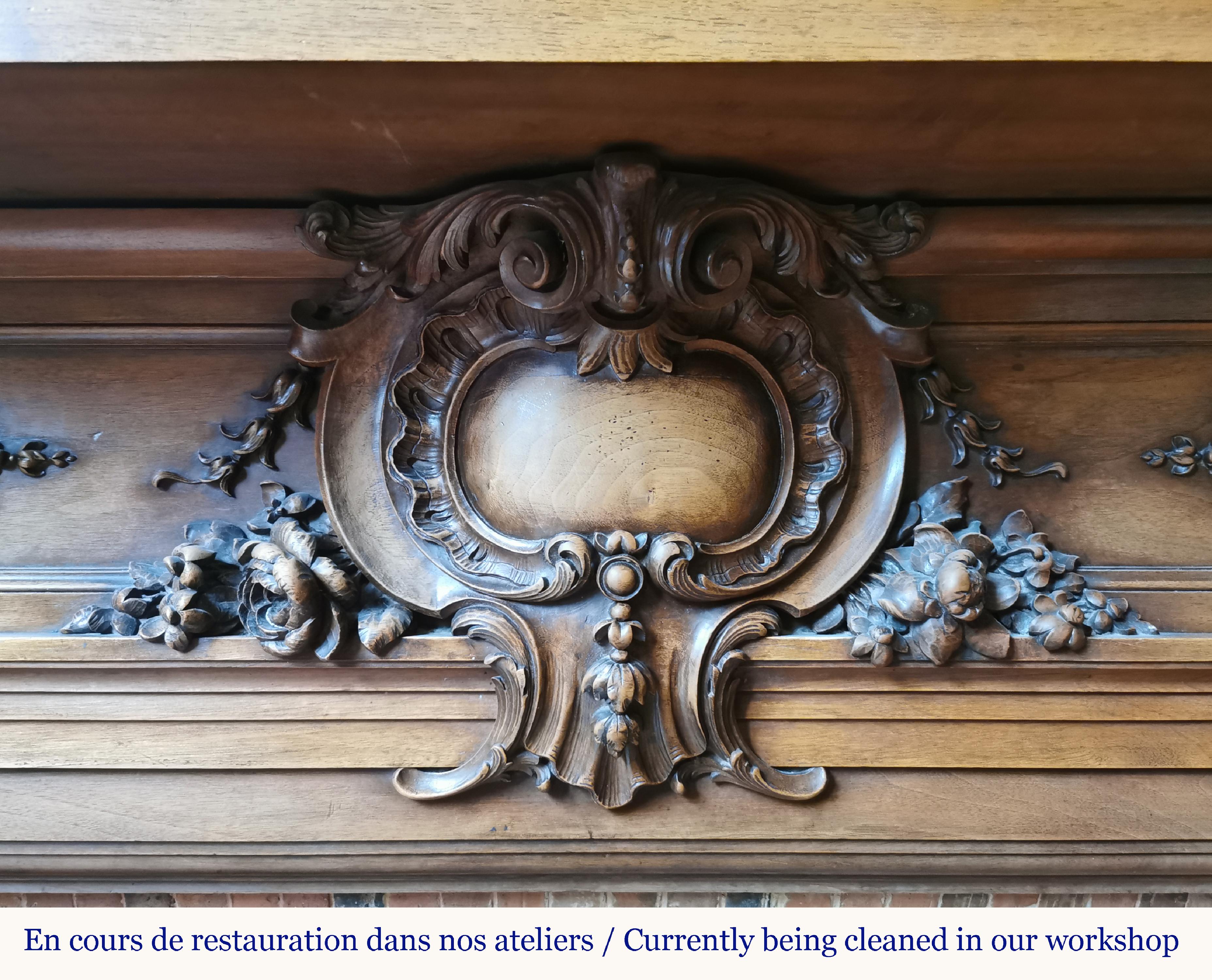 Cette impressionnante cheminée en bois de noyer réalisée dans la seconde moitié du XIXe siècle présente une décoration très riche et éclectique, typique du goût du Second Empire.
Ses jambages roulés sont ornés de visages de lions menaçants à la