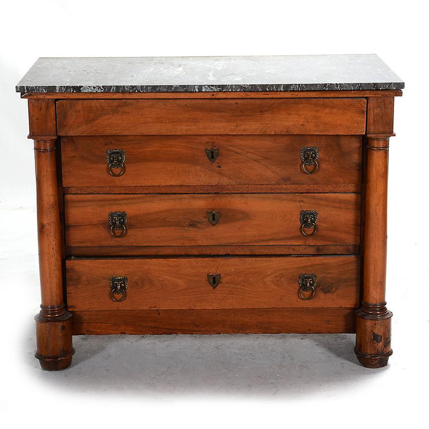 Circa 1810 French Empire (Napoleon)  Empire Walnut Chest of Drawers with a gray marble top; four drawers, three inset with lion head form pulls and shield form escutcheons flanked by pair of iconic columns terminating on a cylindrical base. Retains