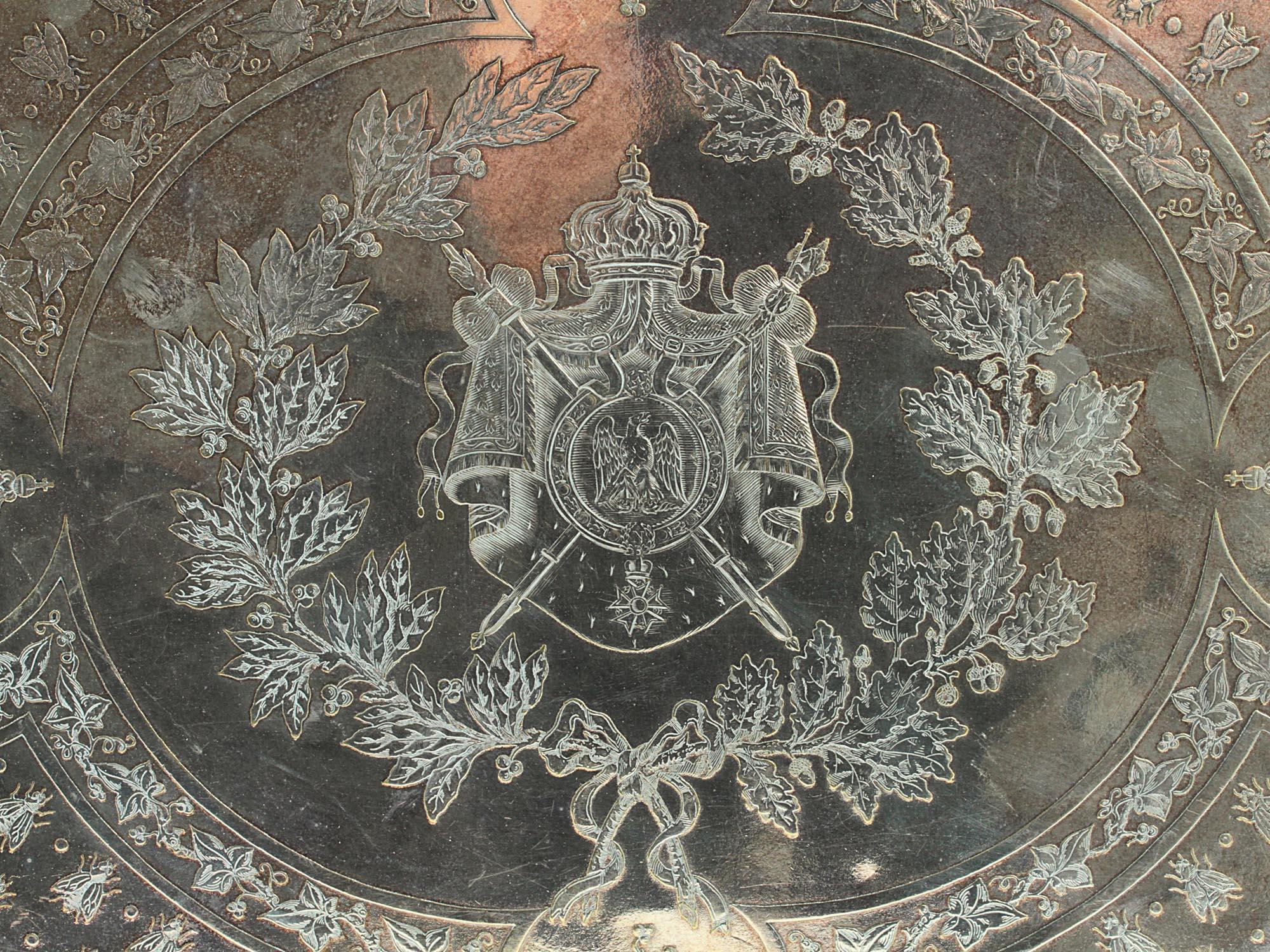 Nuestra bandeja chapada en plata Christofle presenta finos diseños grabados, como el escudo francés, la cifra napoleónica y las abejas imperiales. El reverso tiene la marca del fabricante en cartela ovalada que empieza y acaba con las letras 