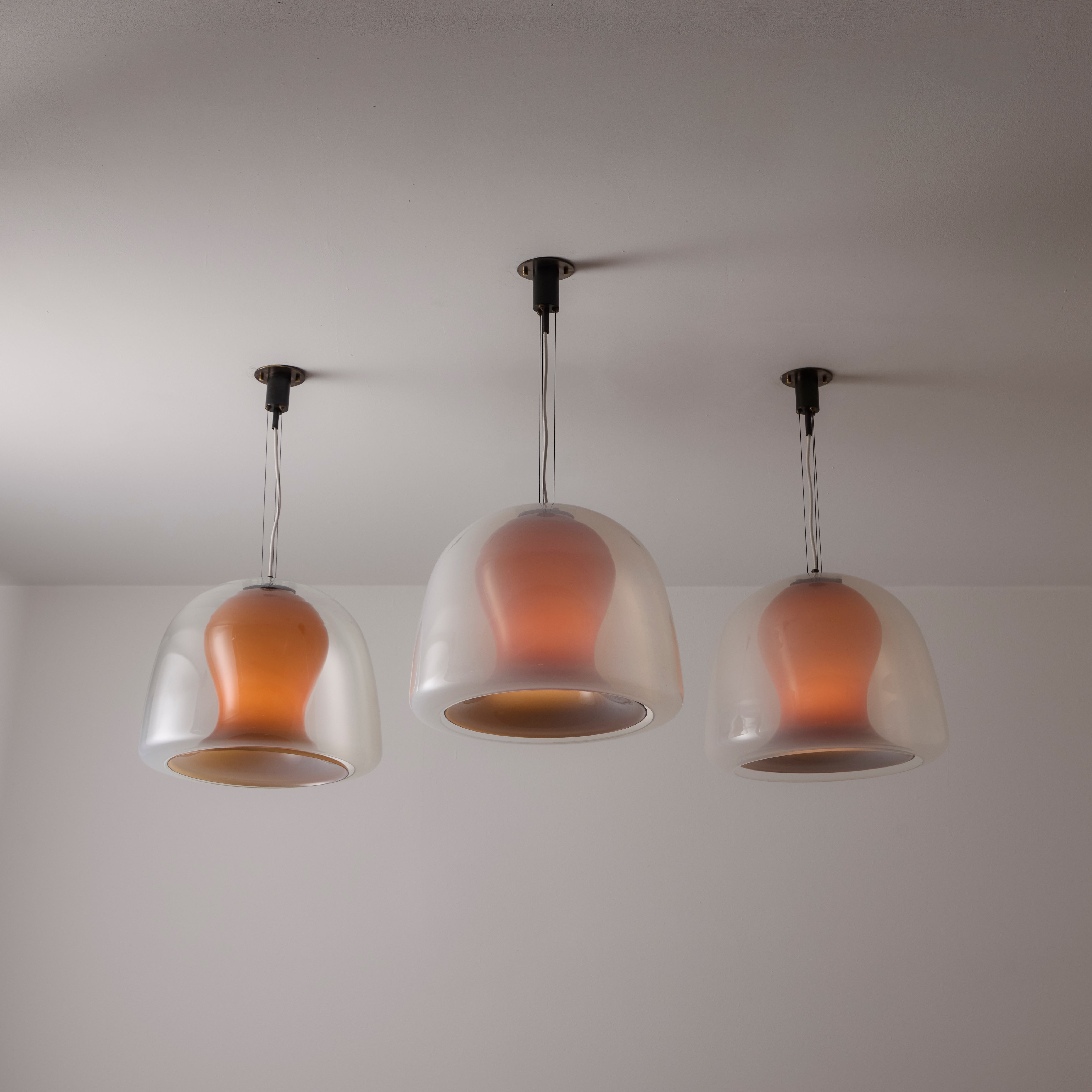 'Naranza' Suspension Lights by Vistosi. Designed and manufactured in Italy, in 1965. Double glass pendants comprising of an inner amber blown glass and an outer clear translucent blown glass. Suspension consists of three steel cables which have