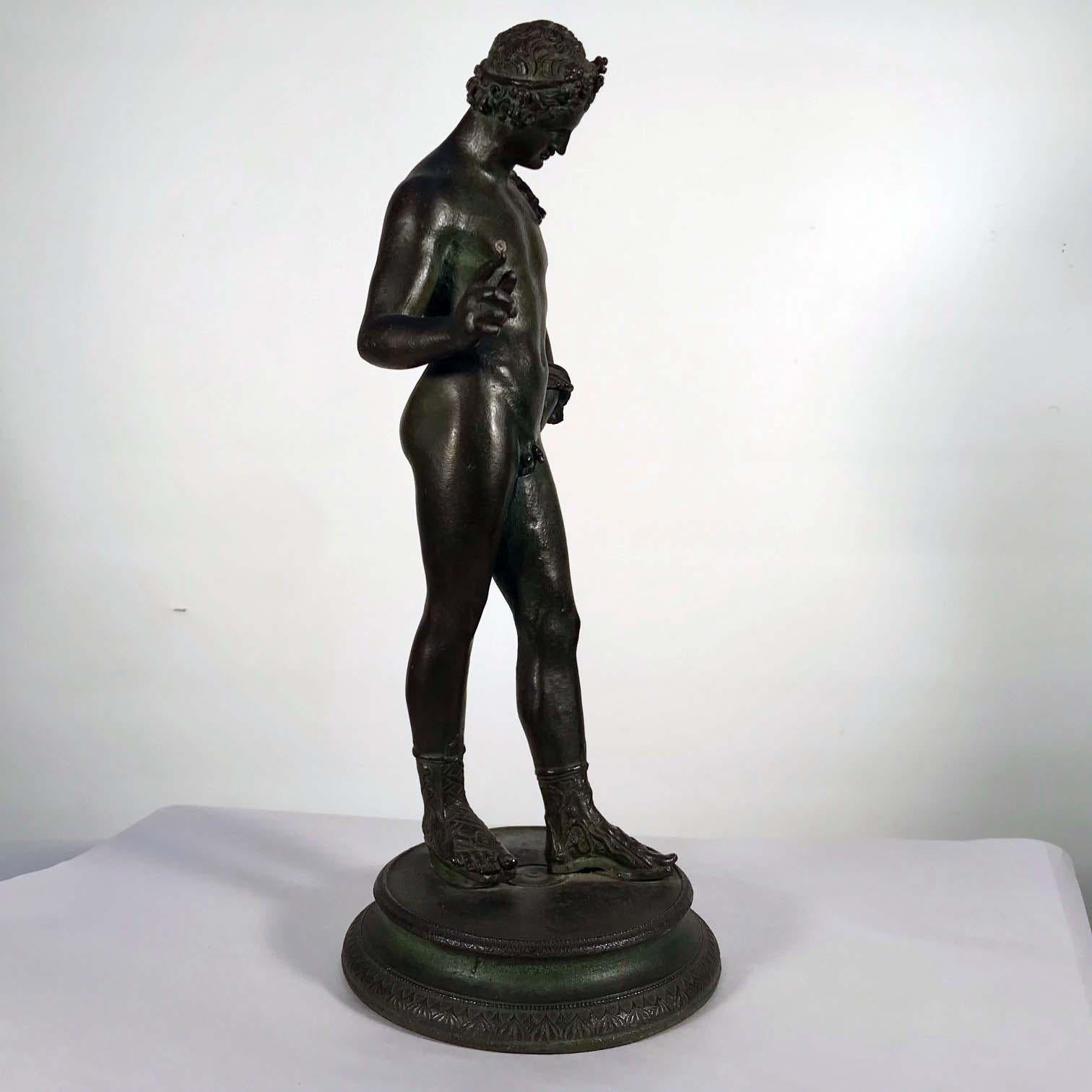 A late 19th century / early 20th century bronze figure of Narcissus, after the Antique, He wears a wreath in his hair and carries a goat skin wine sack and stands on a circular base.
Narcissus was a hunter and known for his beauty. He is said to