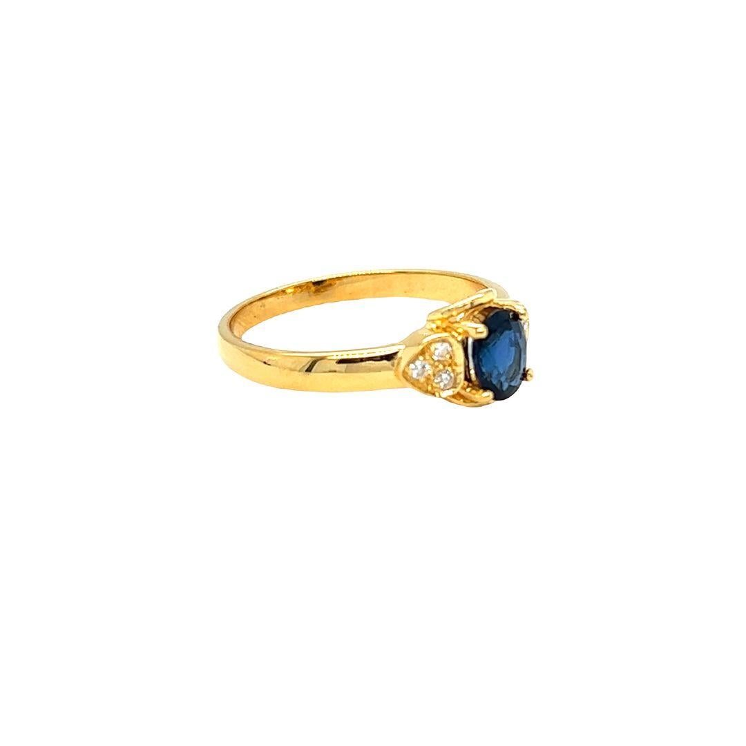 14K yellow gold fashion ring showcases a captivating oval blue sapphire center flower motif. The vibrant blue sapphire measures approximately 6 mm x 4.5 mm, weighing 0.50 carat. On either side of the shank, there are three clusters of diamonds set