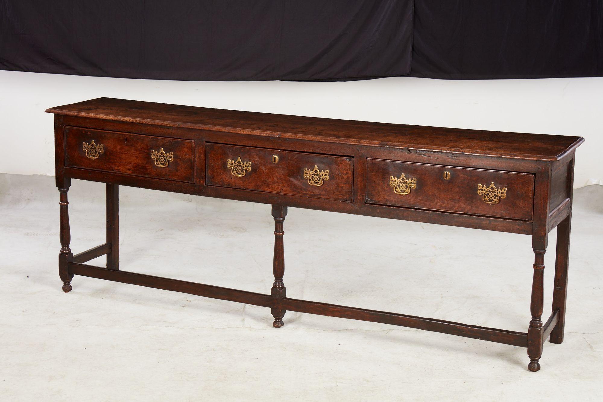 An English 18th century oak sideboard or dresser with long, narrow proportions. Featuring three shallow drawers together spanning the length of the piece, with three turned legs to the front and two straight legs to the back, joined by a long