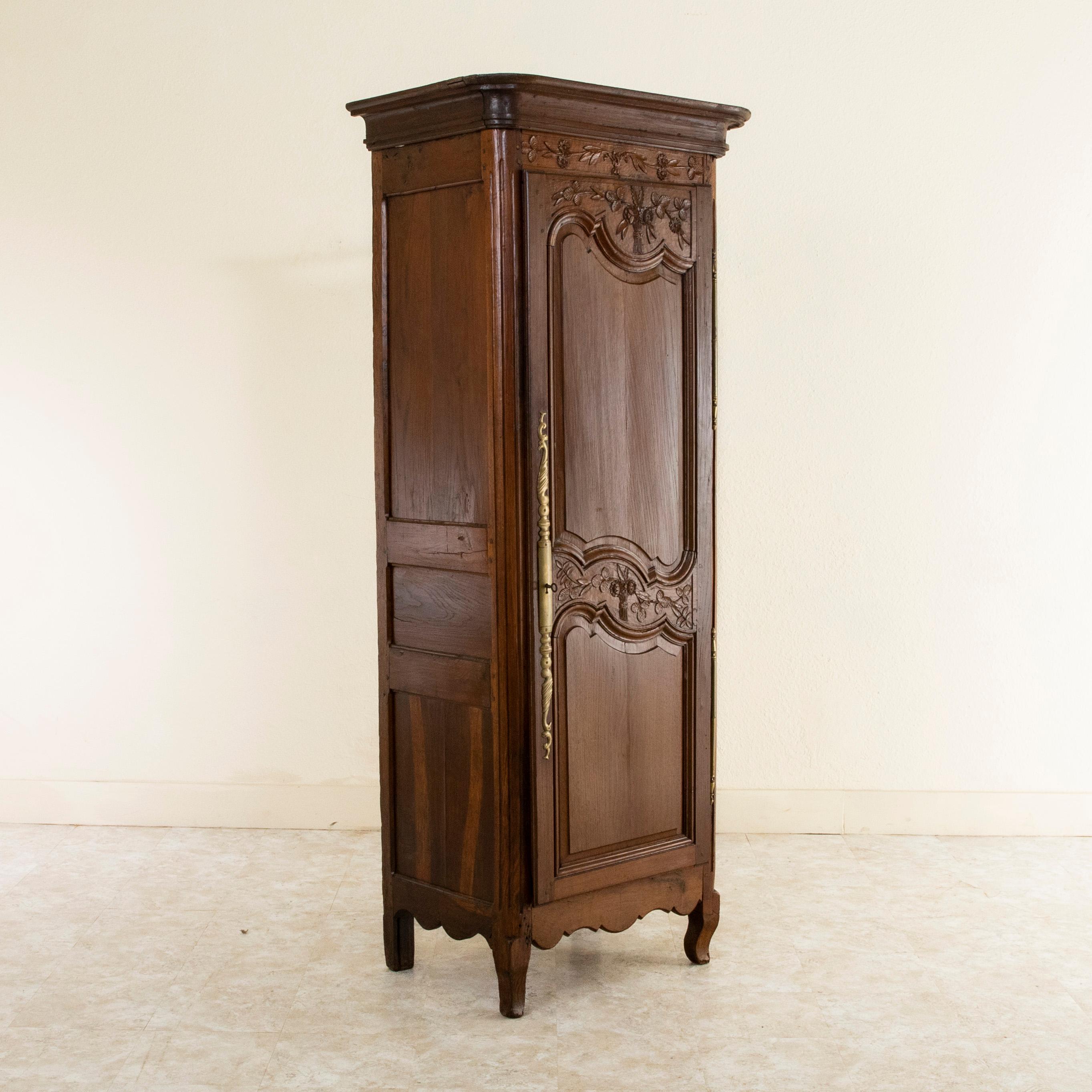 This small scale late 19th century Louis XV style bonnetiere or cabinet from Normandy, France, is constructed of solid oak with hand pegged paneled sides and hand carved detailing of leaves and flowers. Its single asymmetrical door detailed with