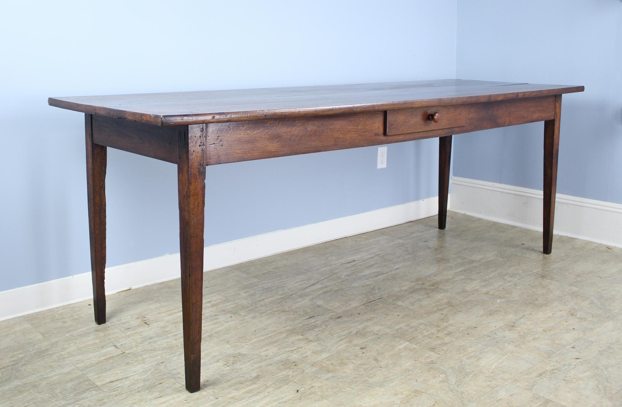A long narrow farm table with glorious color and shine. The chestnut top has interesting grain, and the elegant tapered legs add to the look. The single drawer in the apron lends a nice visual note. There is some age appropriate wear on the left