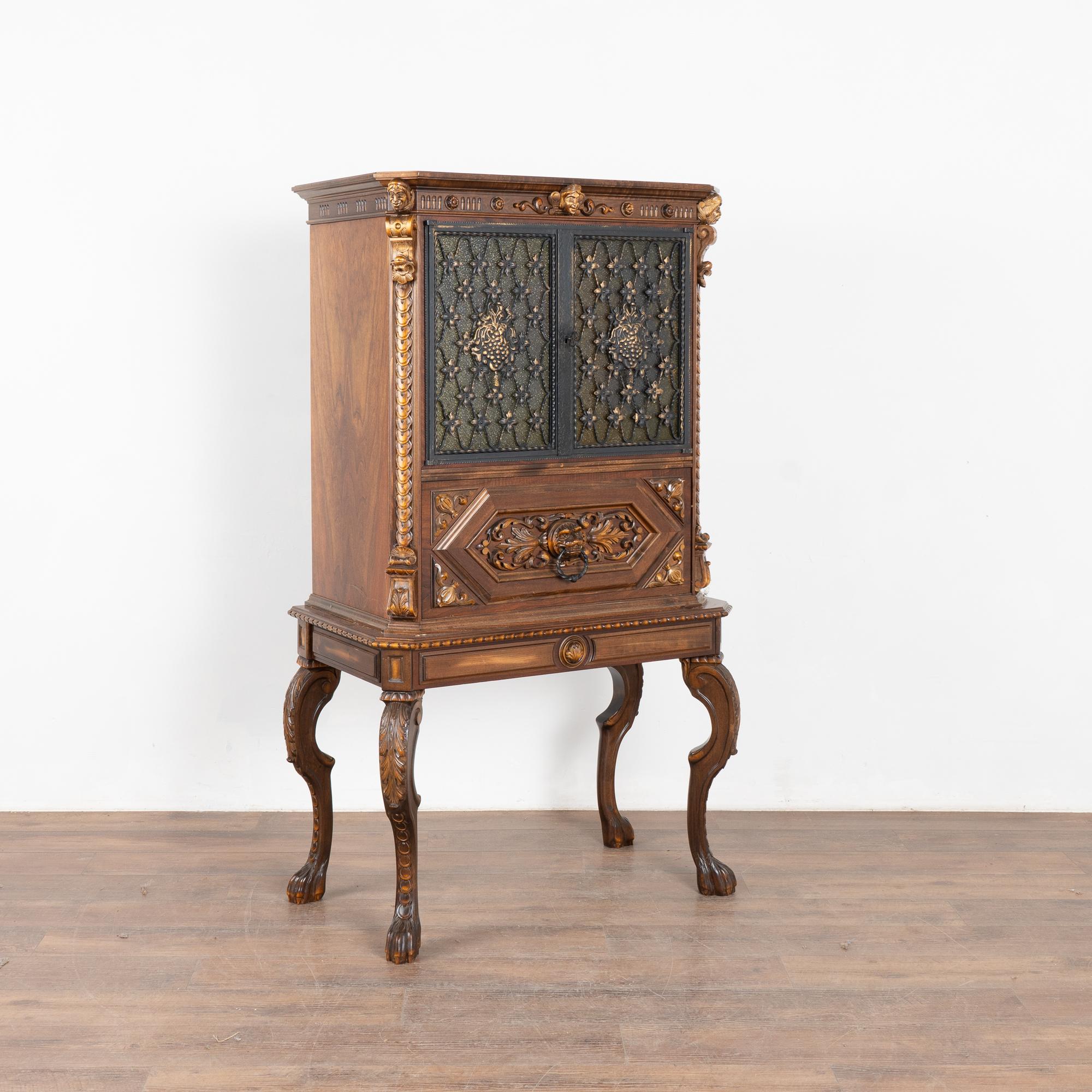 This unique vintage cabinet serves as a small bar with built in glass shelving and interior with colorful family crests/shields covered in glass. Metal grillwork covers the tinted glass panel doors.
Note the unusual lower section, which revolves to