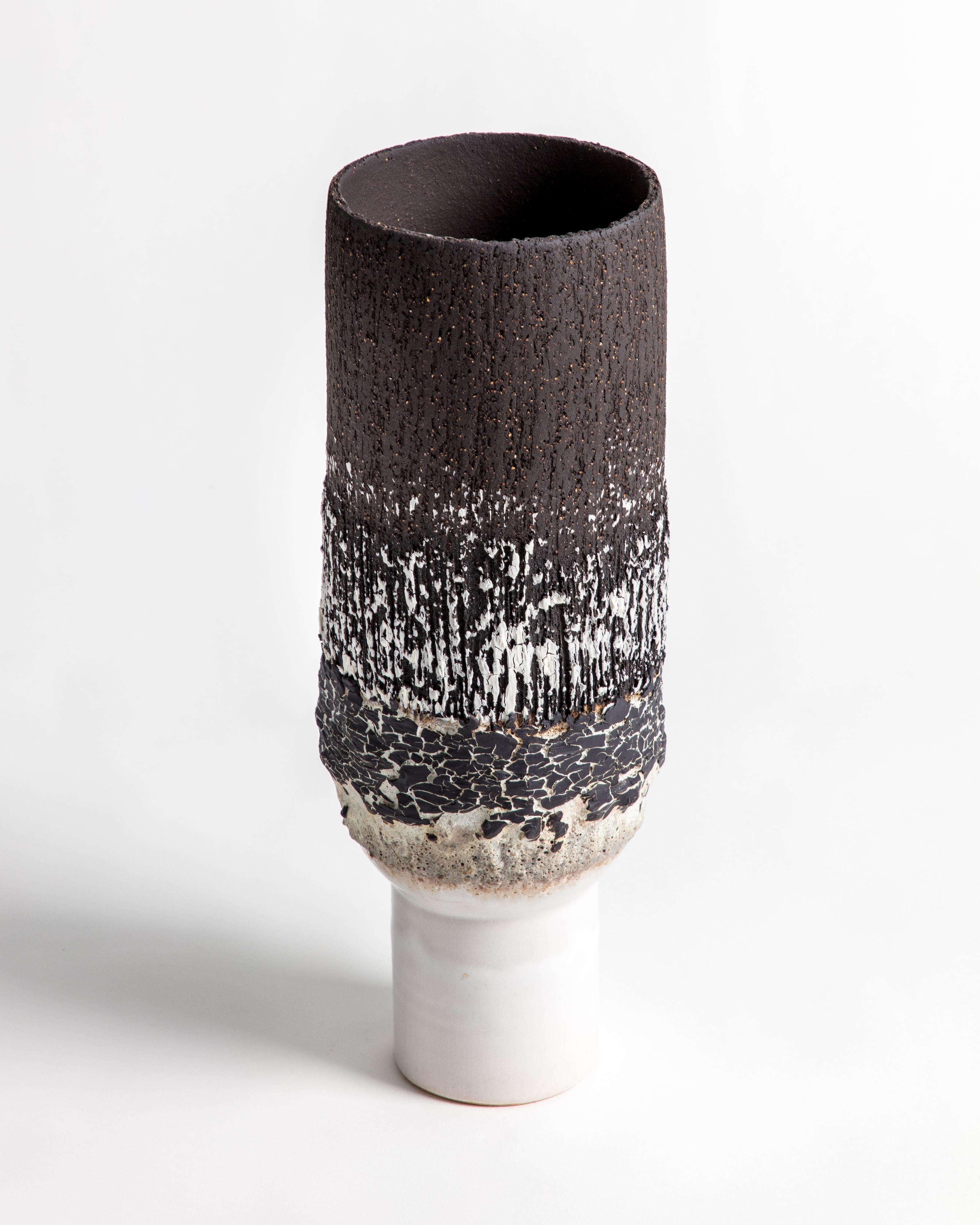 Un élégant vase à piédestal volcanique en grès noir et blanc avec engobe en porcelaine craquelée noire.

L'inspiration pour la pièce vient de l'argile elle-même et des relations chimiques que la glaçure et la matière volcanique créent. Voyages