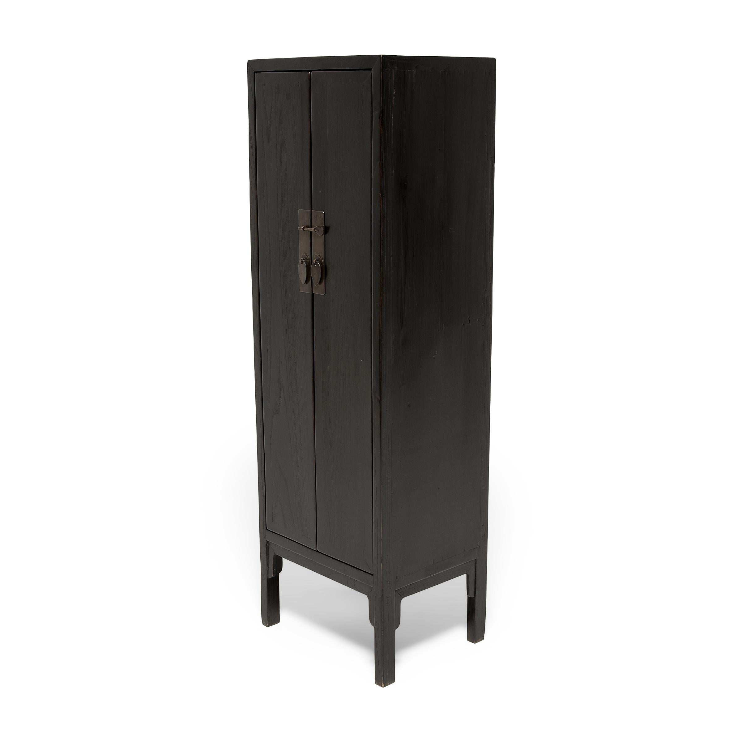 This upright cabinet from northern China has a timeless and minimal design that blends into any interior. The narrow cabinet has a simple, angular form with square corners, straight legs, and elongated doors that run the full length of the cabinet