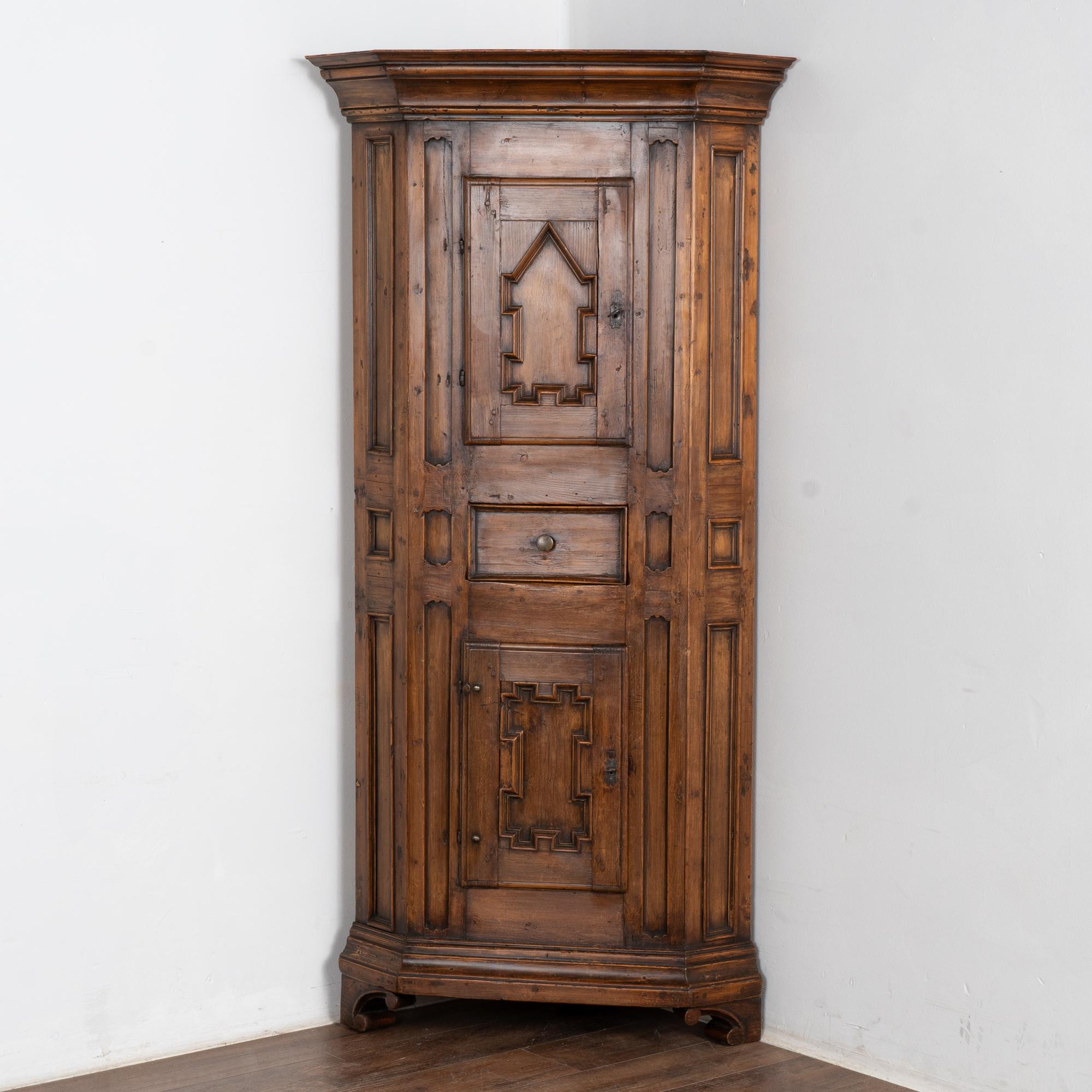 Questo stretto mobile ad angolo in pino ha due ante a pannelli separate da un cassetto centrale. La patina scura e ricca del pino riflette la sua età.
Restaurata, forte e stabile, questa credenza angolare è stata incerata ed è pronta per essere