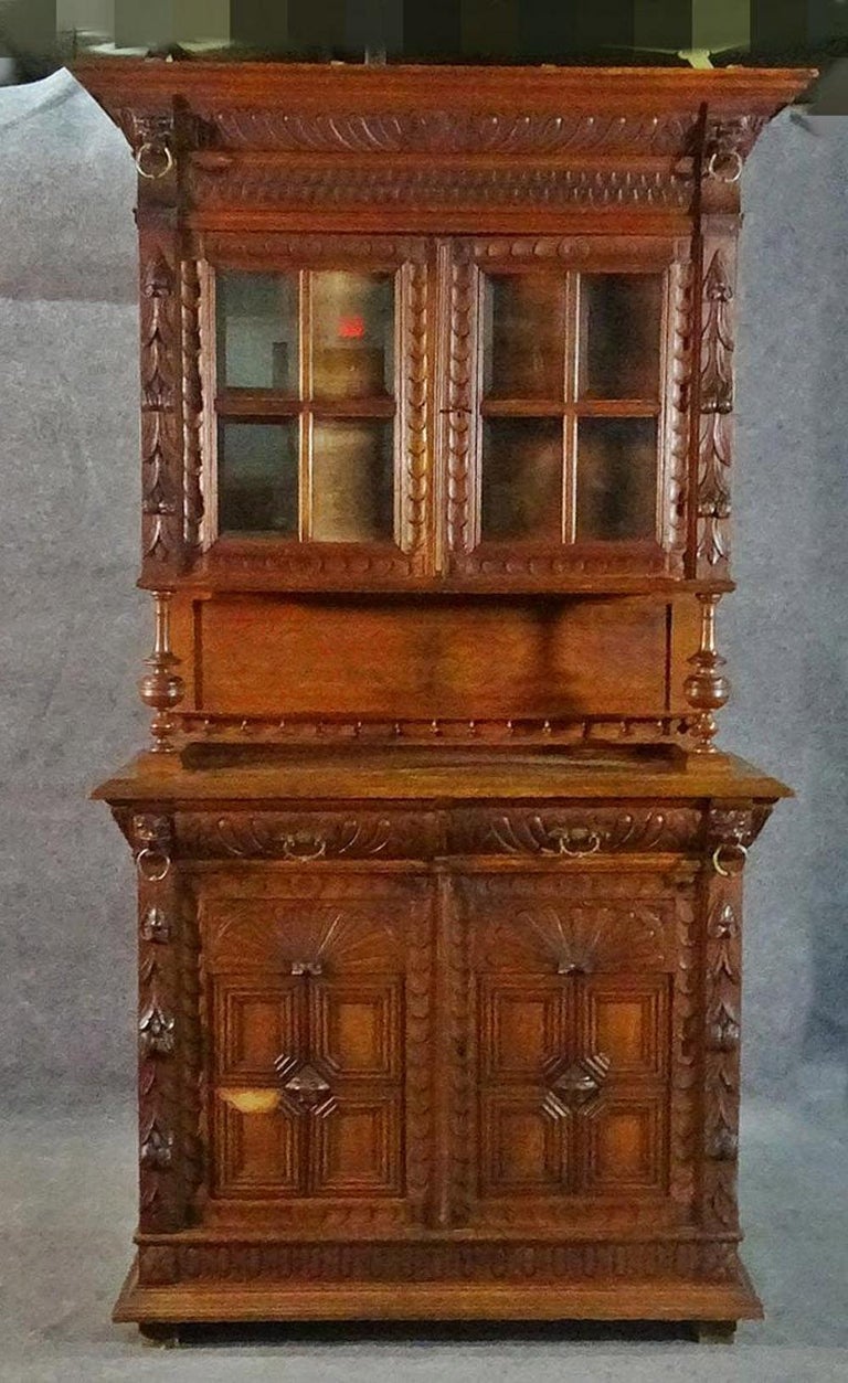 Great narrow size! Perfect for an apartment in NYC. Comes as two pieces. Carved. Oak. Top has 2 glass doors containing one shelf. 2 drawers. Bottom has 2 doors containing one shelf. Metal hardware. 87 1/2