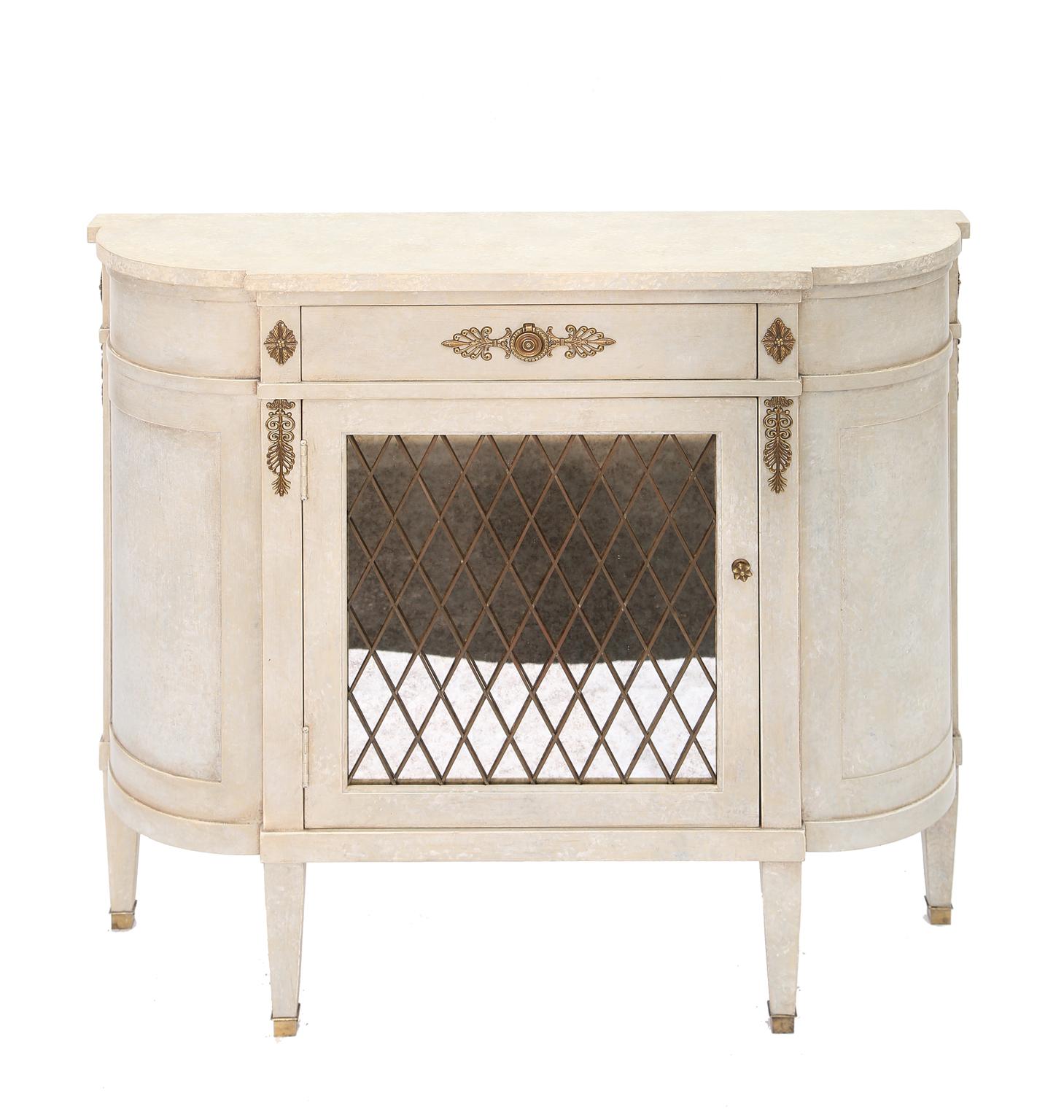 Commode, in demilune shape, having a painted finish with natural wear, its single drawer over cupboard door covered in old mirror with brass crosshatch overlay; raised on square tapering legs.

Stock ID: D4100.