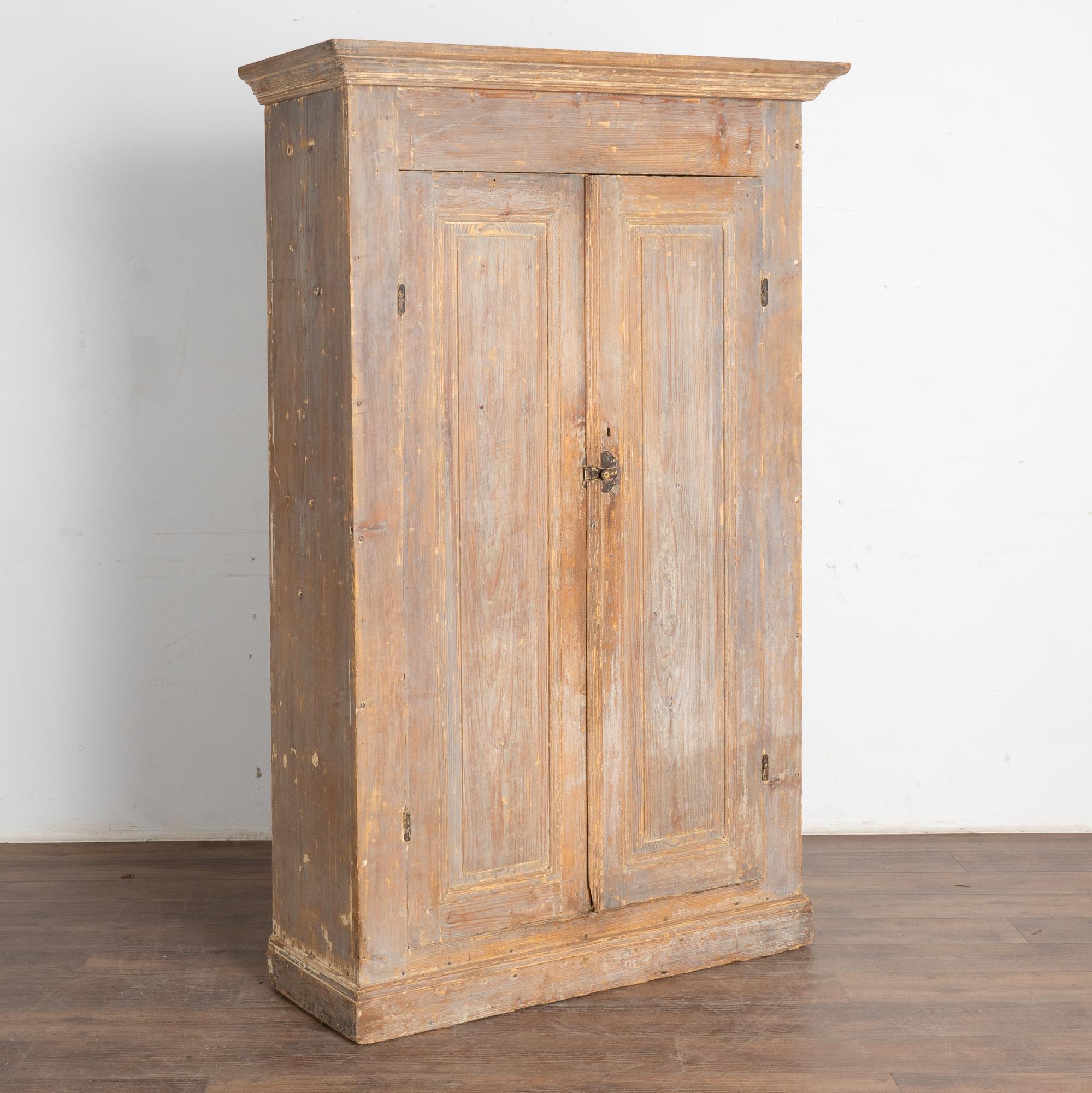 This narrow armoire shows off the clean lines of its Swedish country styling and stands just over 6' tall. 
The original hand-painted gray finish is now faint, worn down to reveal the warm patina of natural pine that is a result of generations of