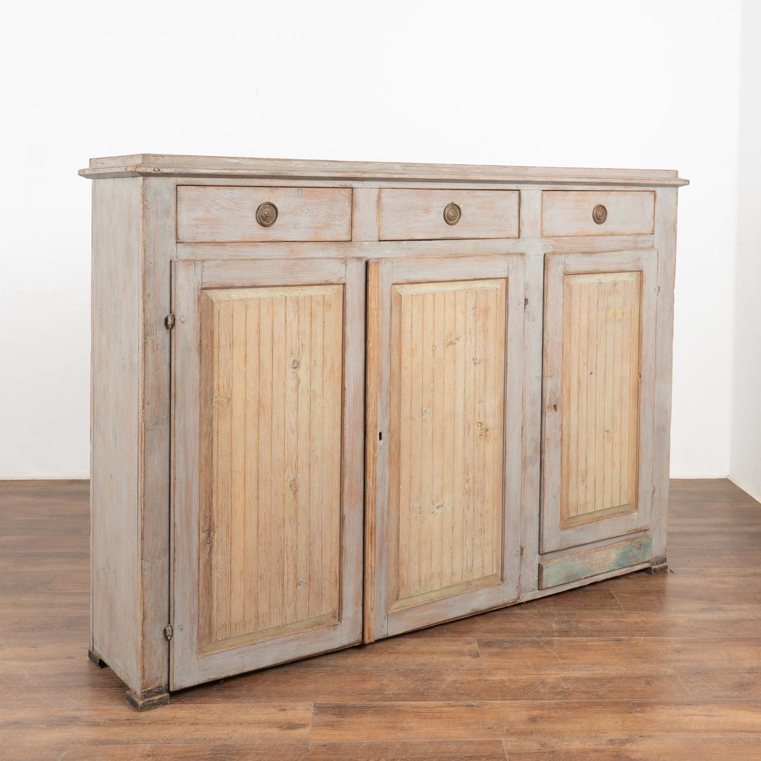 Swedish country 4' tall pine sideboard with original pale blue/gray painted finish. Three simple grooved panel doors with contrasting antique white painted finish, all lightly distressed through generations of use. 
Please refer to photos of 