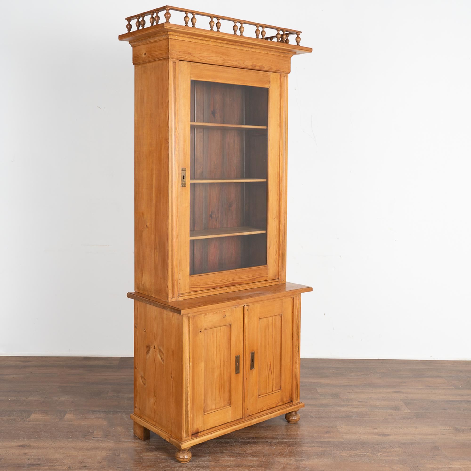 Narrow pine display cabinet or bookcase with fluted side trim, bun feet and finials forming crown. 
Interior shelving creates easy display of books or collectibles, while the 33