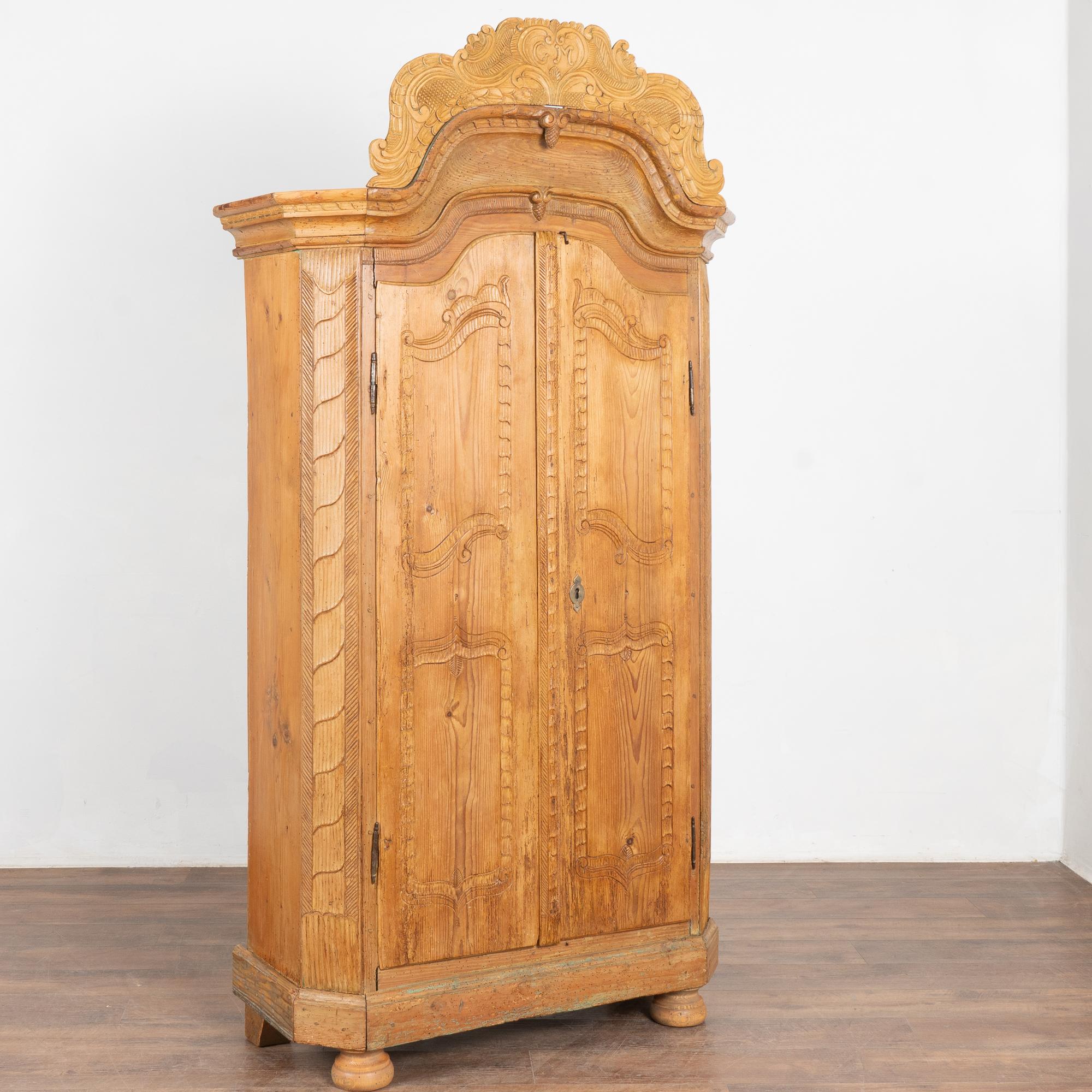 Decorative carving in the panels and crown add a sophisticated touch to this small two door pine armoire with an aged patina from years of use.
The doors are held in place by a small exterior metal latch; no lock nor key remain. 
Restored, this