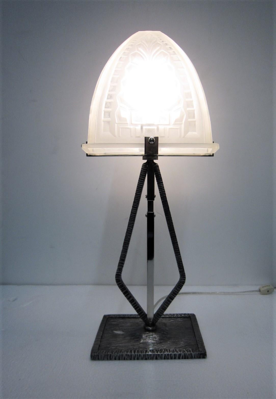 A French Art Deco or Minimalist unusually shaped, narrow table lamp featuring a heavily molded French art glass
trapezoidal shade of stylized fern and geometric design, resting on a nickeled finish hand-hammered iron base with nickeled bronze trim.