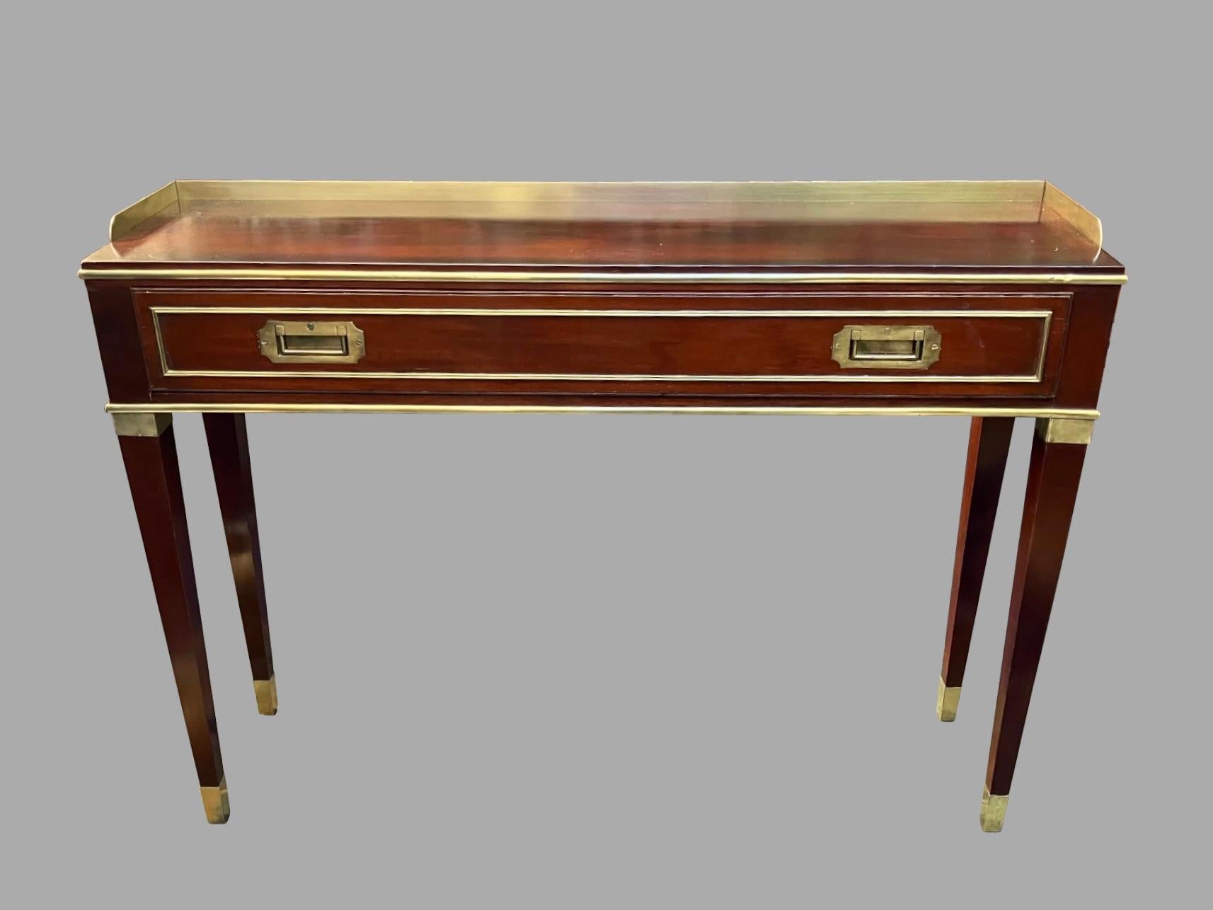 An elegant English mahogany campaign style brass mounted console or sofa table, of unusually narrow proportions, possibly a custom made piece for a yacht, the top with a solid brass gallery above a long frieze drawer fitted with two recessed