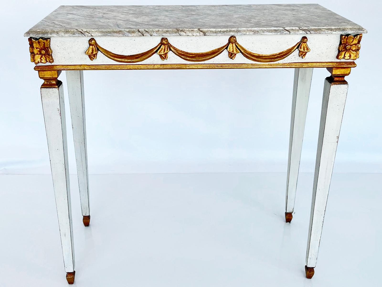 Narrow console table, painted and parcel gilt, having a molded, rectangular top of faux painted marble, on fielded apron outcarved with gilded swags, square block rosettes adorn each corner, over four square-section, tapering legs, ending in gilded