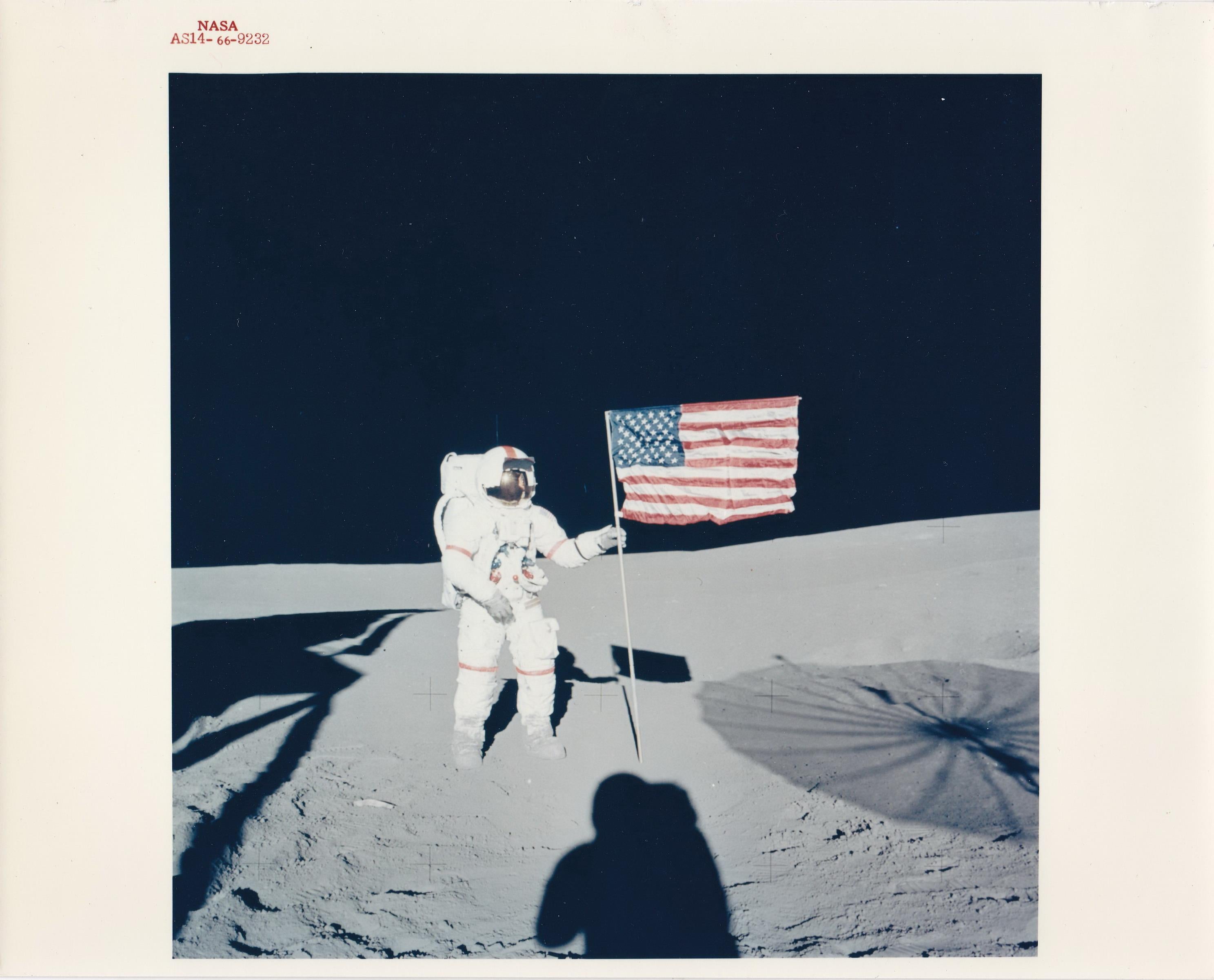 Alan Shepard, commandant d'Apollo 14 de la NASA, se tient près du drapeau américain sur la Lune, avec l'ombre d'Edgar D. Mitchell, pilote du module, qui prend la photo. 

Il s'agit d'une photographie chromogène vintage de 8" x 10" sur papier fibre,