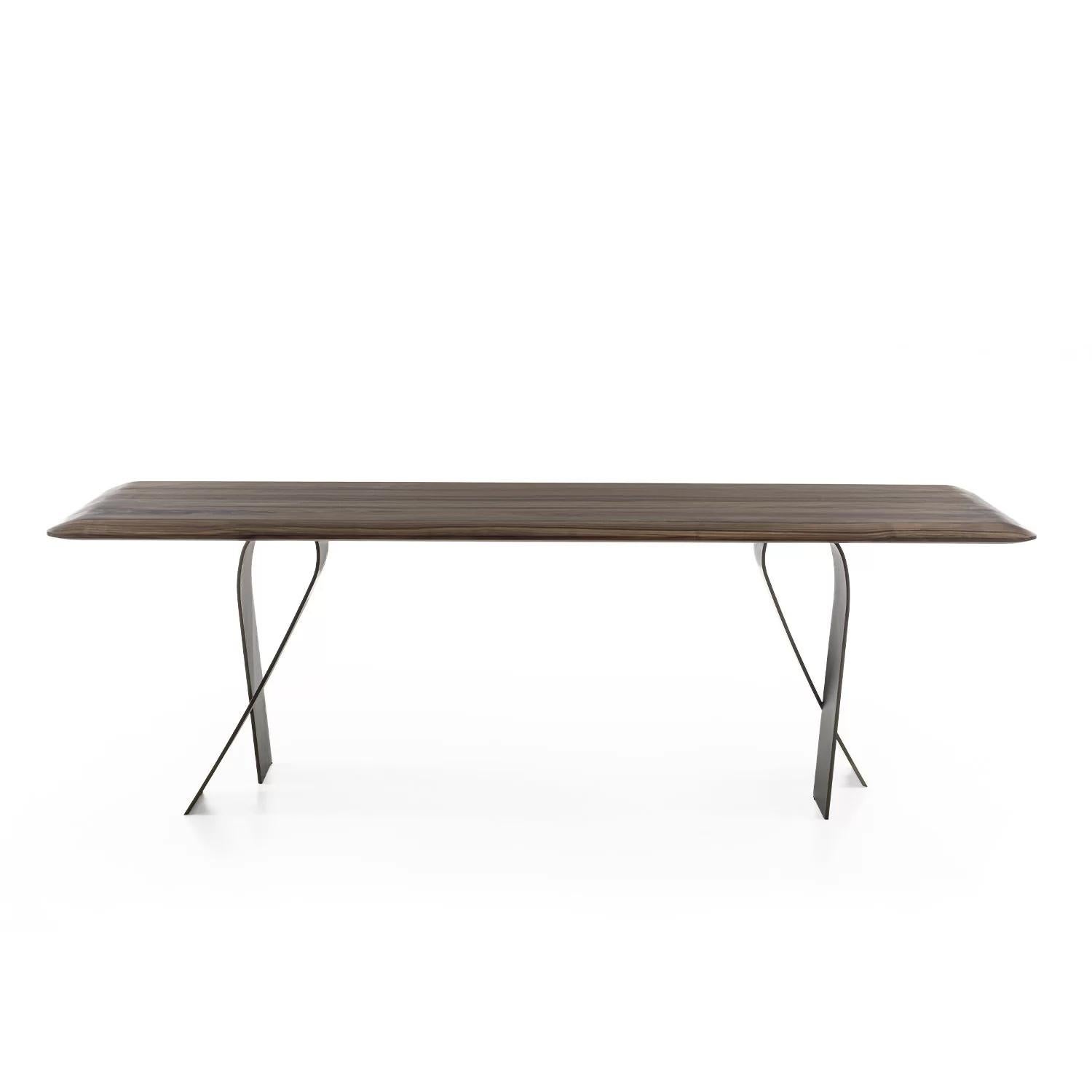 Tisch mit einer Platte aus Massivholz mit verleimten Leisten, der sich durch eine geringe Dicke auszeichnet, dank der abgeschrägten und abgerundeten Kanten, die ihm ein leichtes und gewundenes Design verleihen, gepaart mit gewundenen Eisenbeinen,