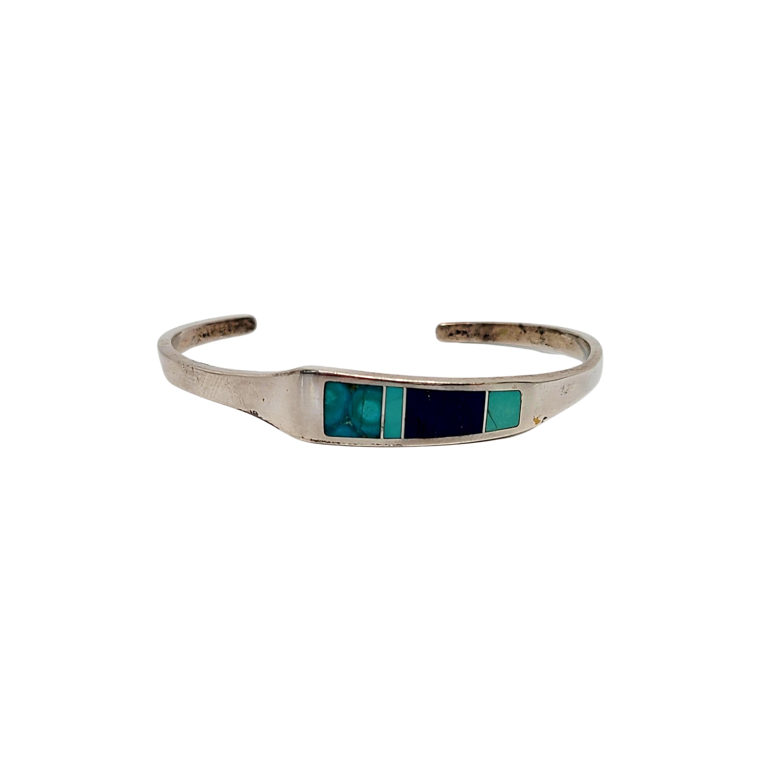 Sterling silver and multi-stone inlay cuff bracelet by Native American Navajo artisans, Ray Tracey and Knifewing Seguara.

Beautiful channel inlay mosaic of what appears to be turquoise and lapis lazuli stones. A collaboration of well known