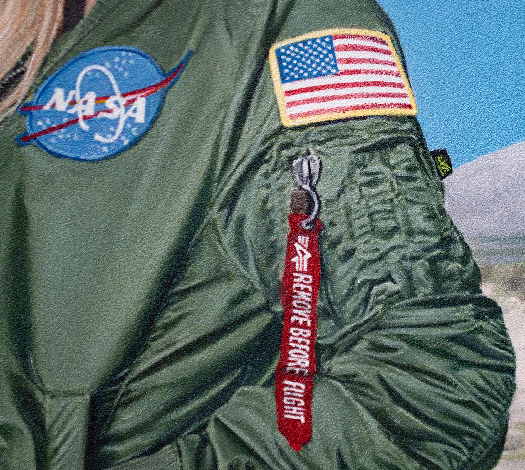 La figura central, vestida con una chaqueta de bombardero de la NASA, encarna la ambición y la valiente persecución de los sueños. Su postura segura y equilibrada contrasta con el movimiento dinámico de los aviones de combate que planean por encima